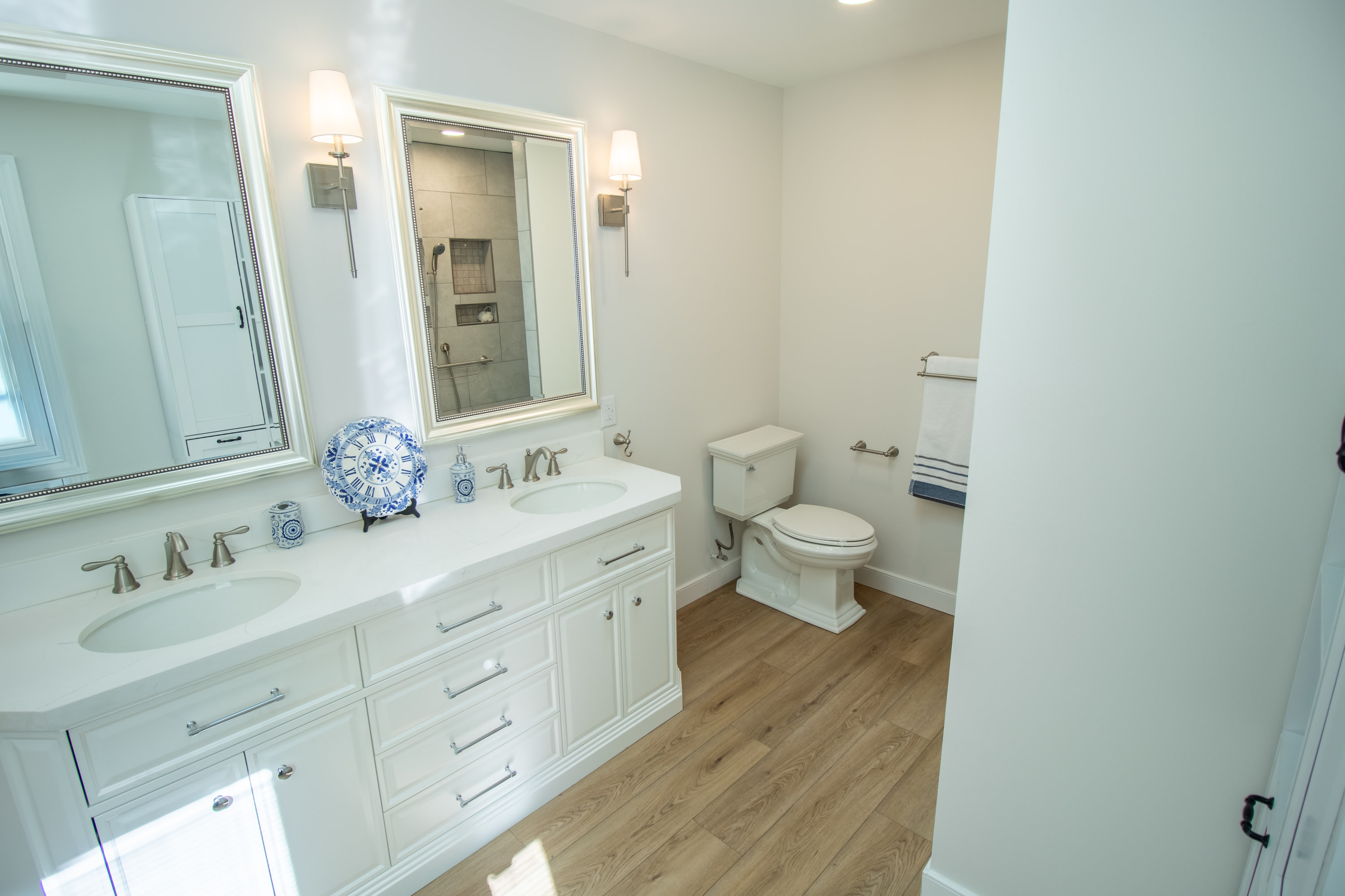 Double-sink bathroom vanity with brushed nickel faucets, toilet, and mirror reflection of tiled shower.