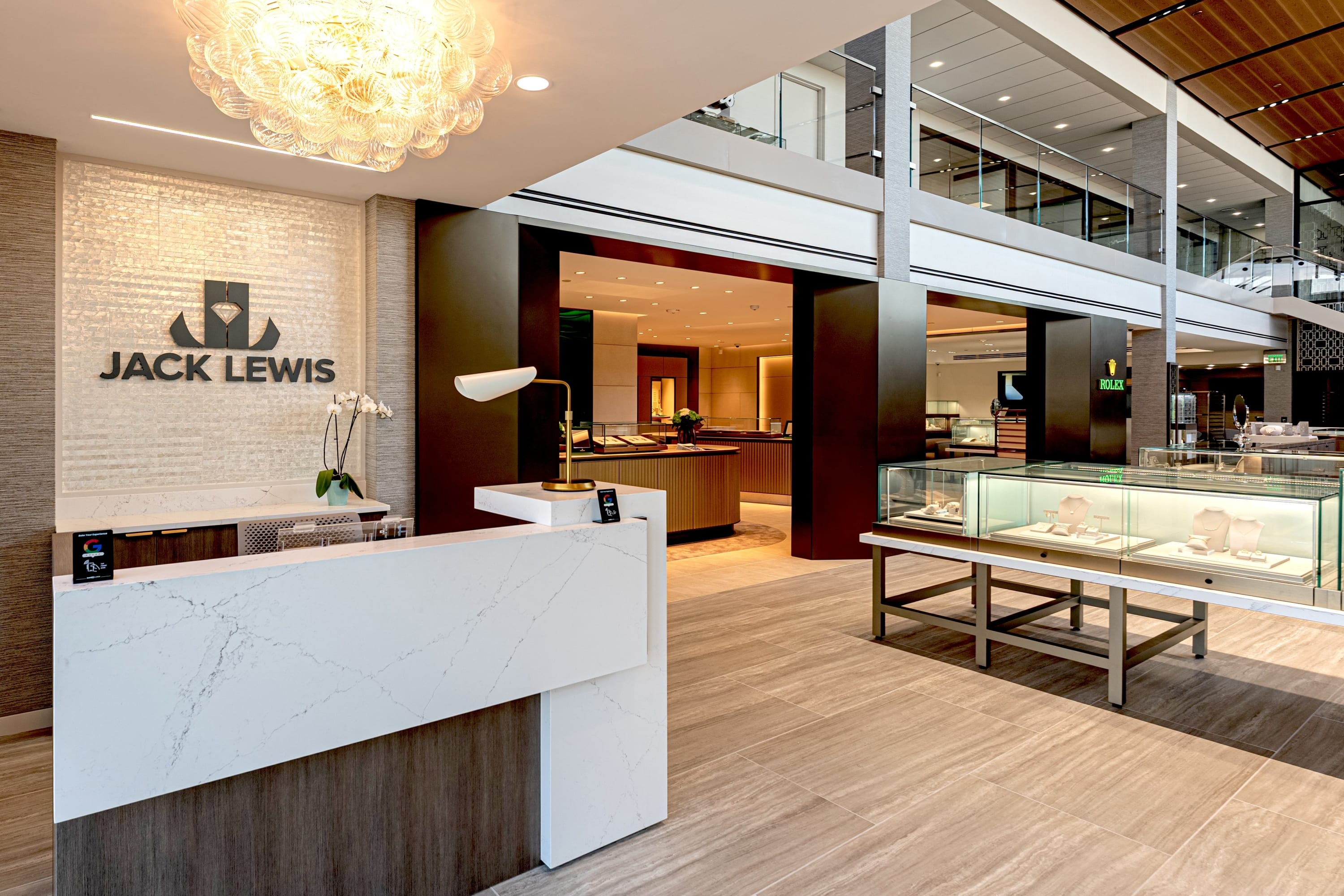 Reception area inside Jack Lewis Jewelers featuring a modern marble desk, illuminated logo wall, and luxury jewelry displays.