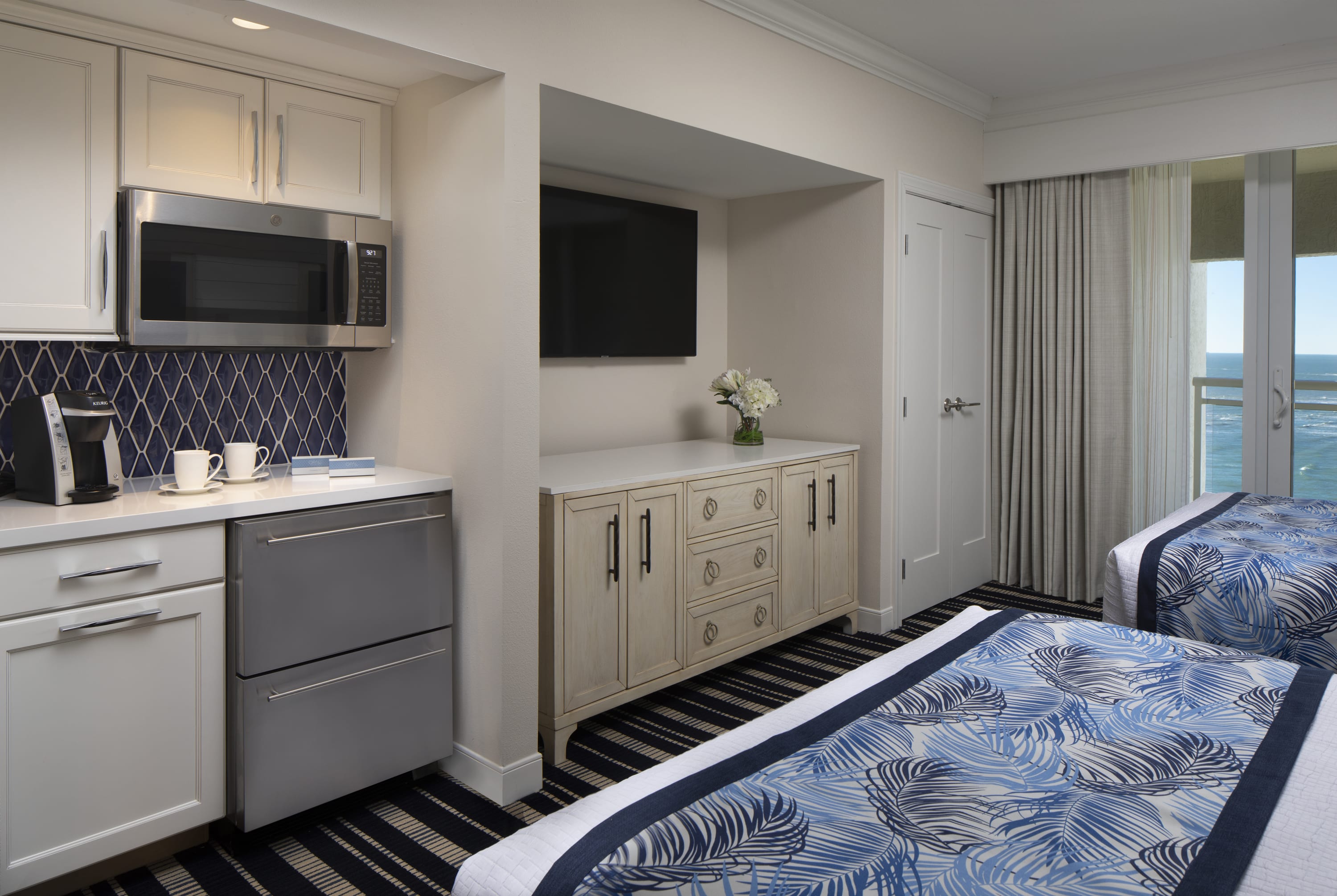 Two Queen beds across from a wet bar, a small refrigerator, a microwave, and TV mounted on the wall above a dresser
