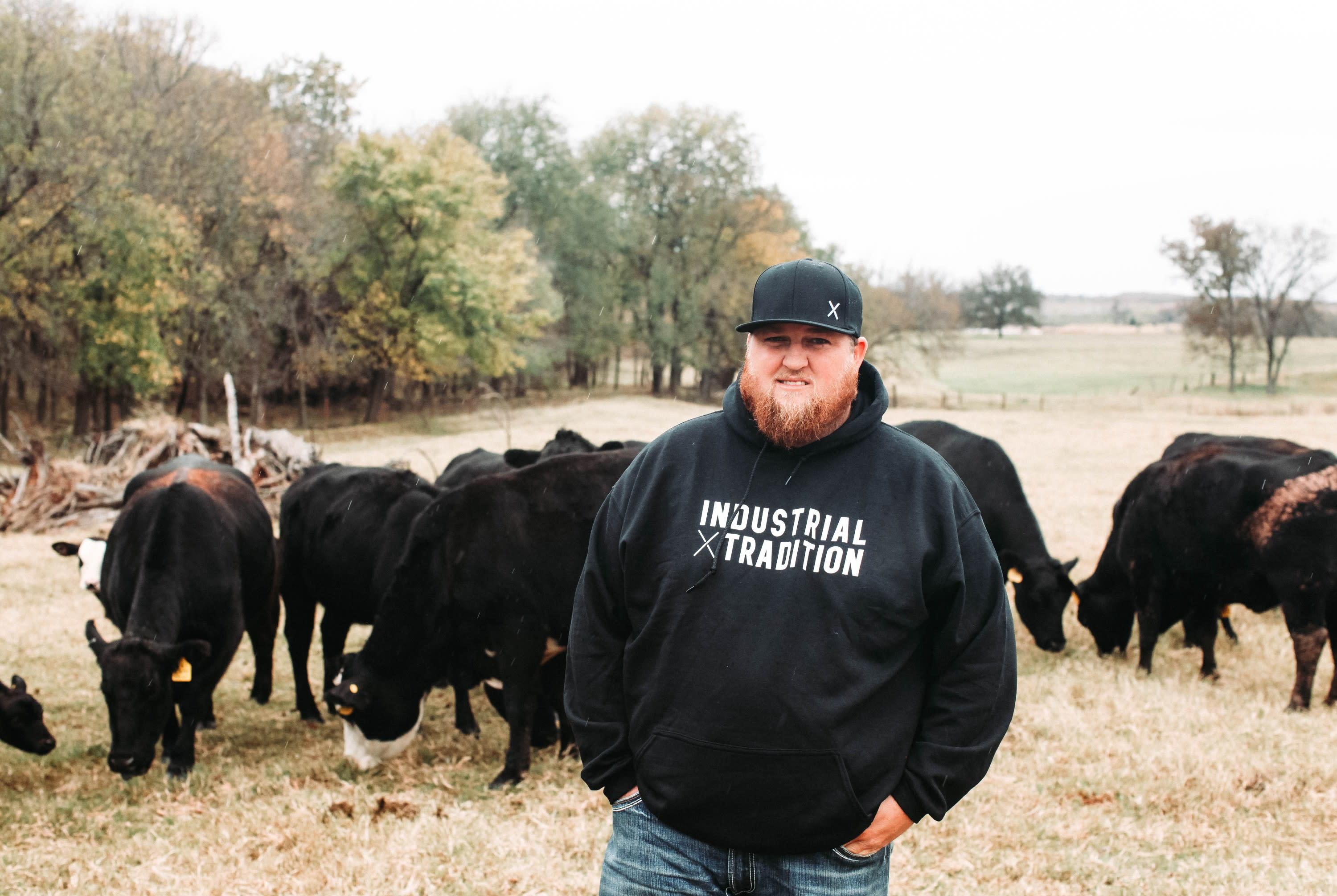 Industrial Tradition cap and hoodie on man standing in front of cattle