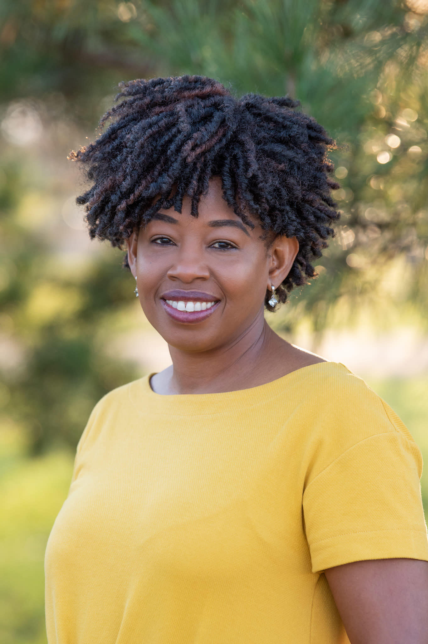 An African American woman dressed in yellow dress at a park smiling for her headshot session