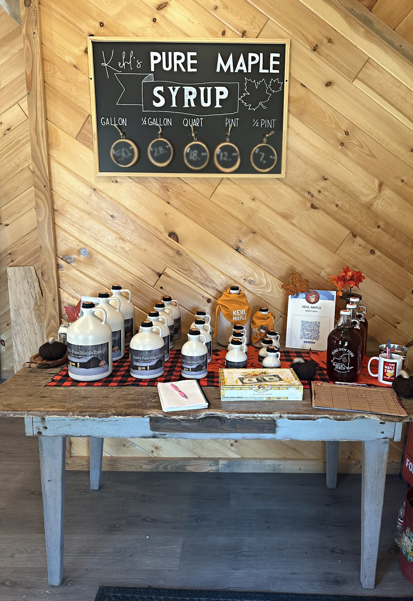 Photo of a table with various sized maple syrup bottles and a sign on the wall behind explaining the sizes.