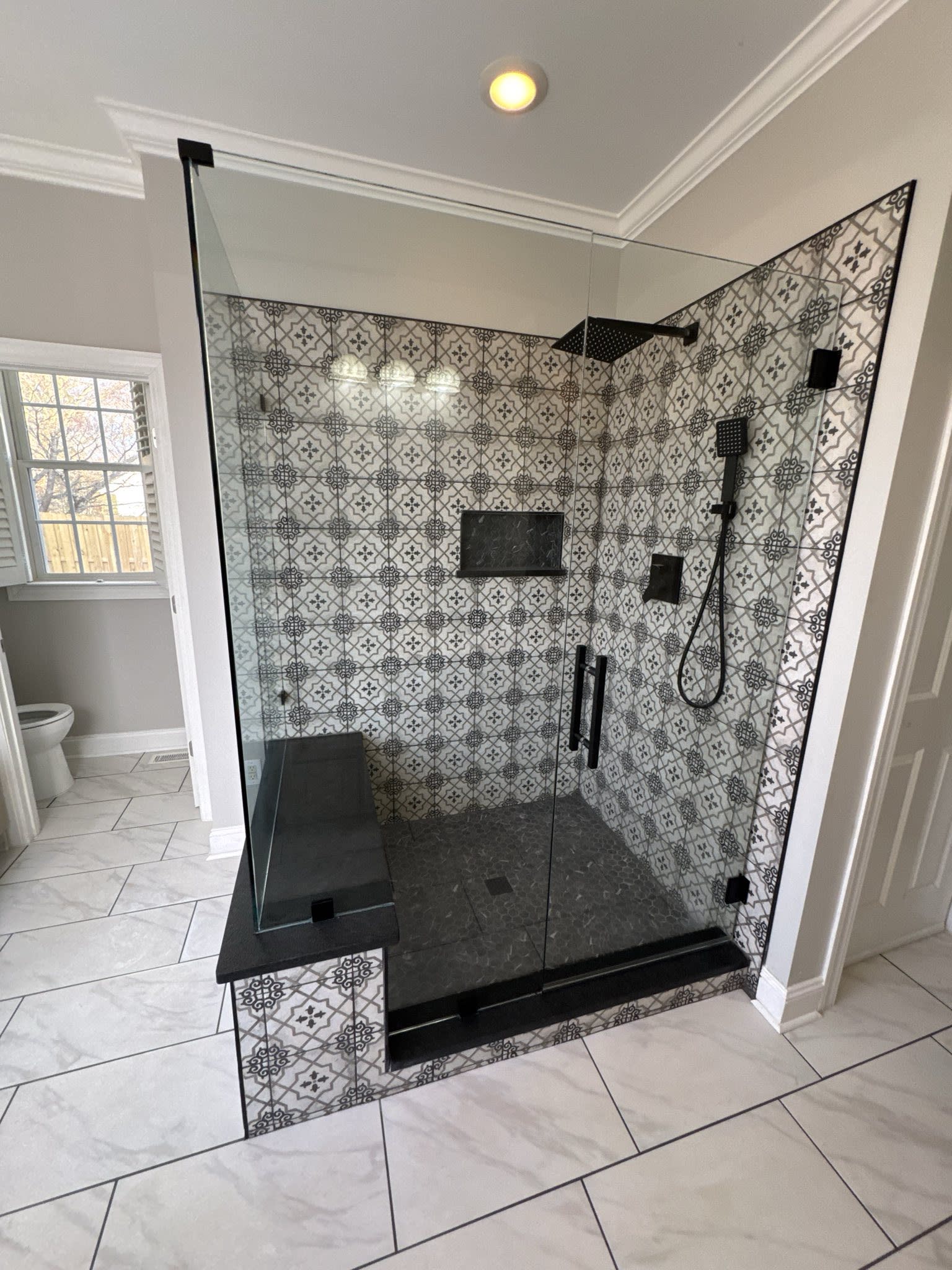 90 Degree frameless shower enclosure over beautiful tile pattern with matte black hardware.