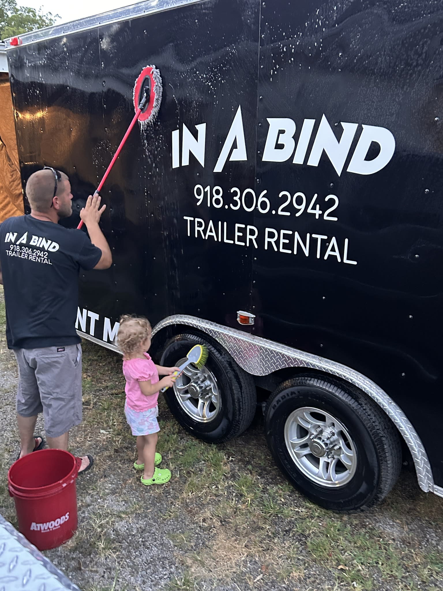 In A Bind Trailer Rental Cleaning "Crew" - Photo shows a man and a toddler cleaning an enclosed trailer.