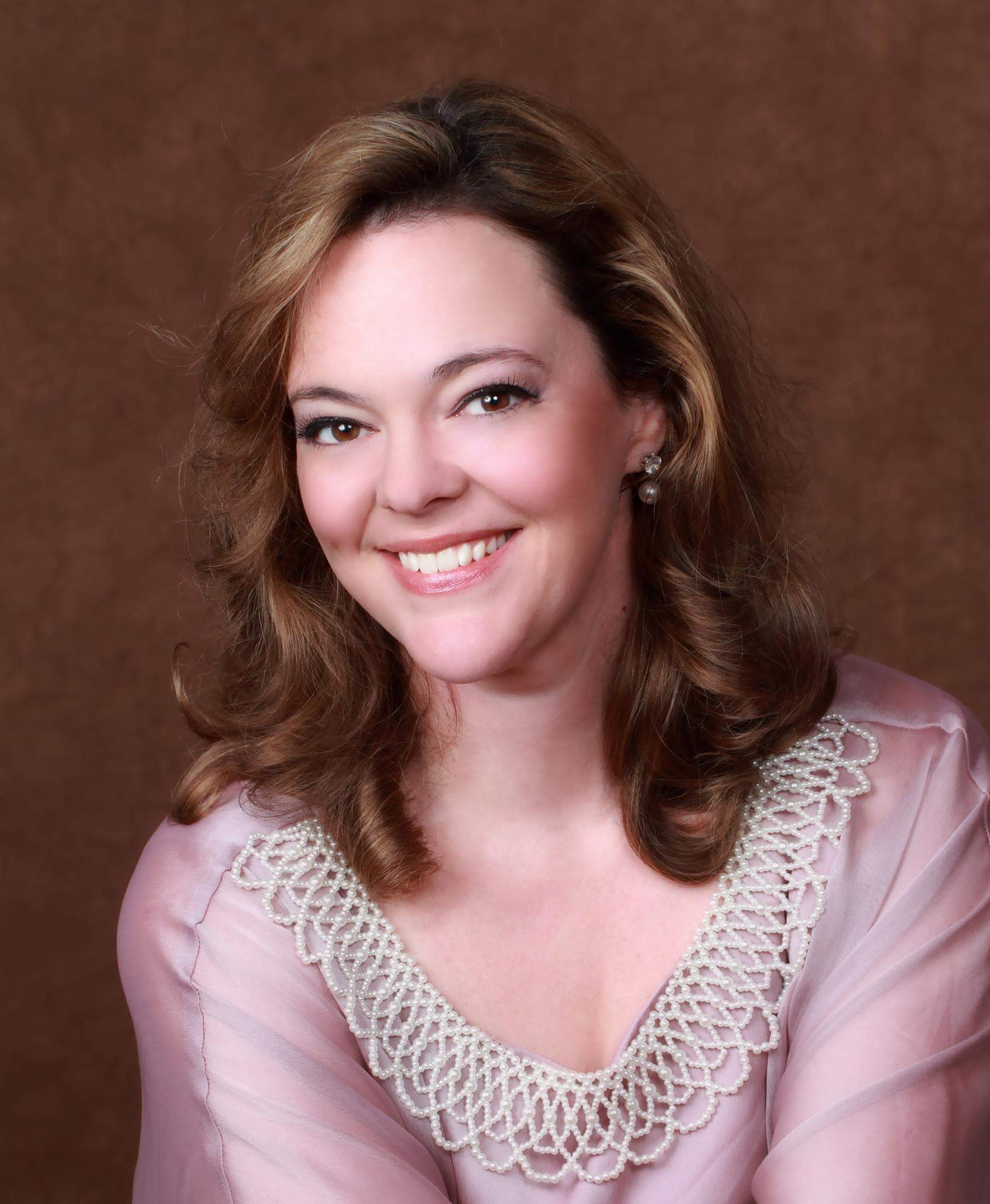 portrait of woman with long brown hair, wearing a pink blouse