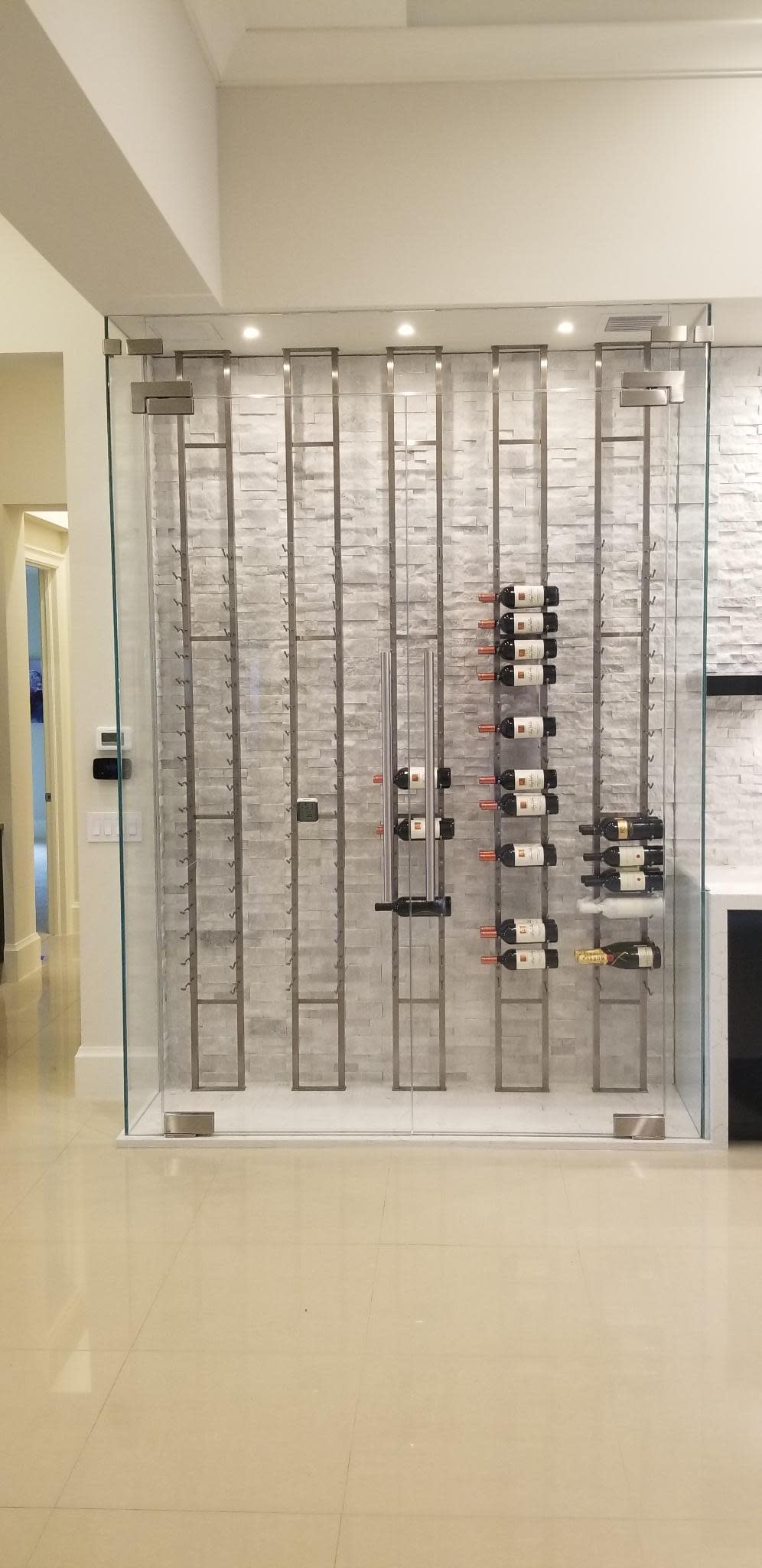 Sleek frameless glass wine enclosure with pivot hinged doors and brushed stainless patch fitting hardware.