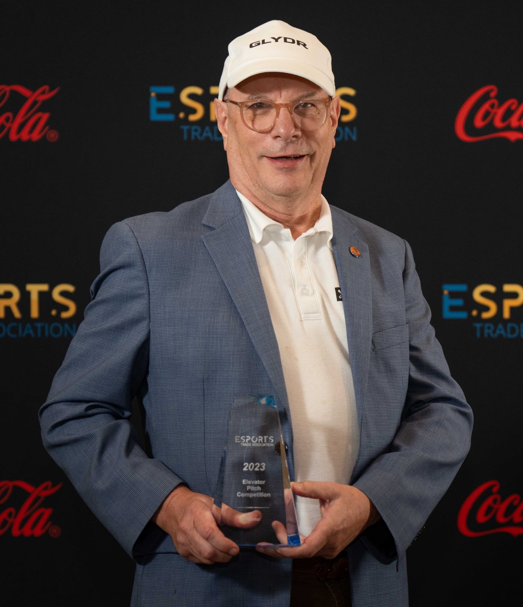 Rick Tett holding the Elevator Pitch winner's trophy in front of the Esports banner