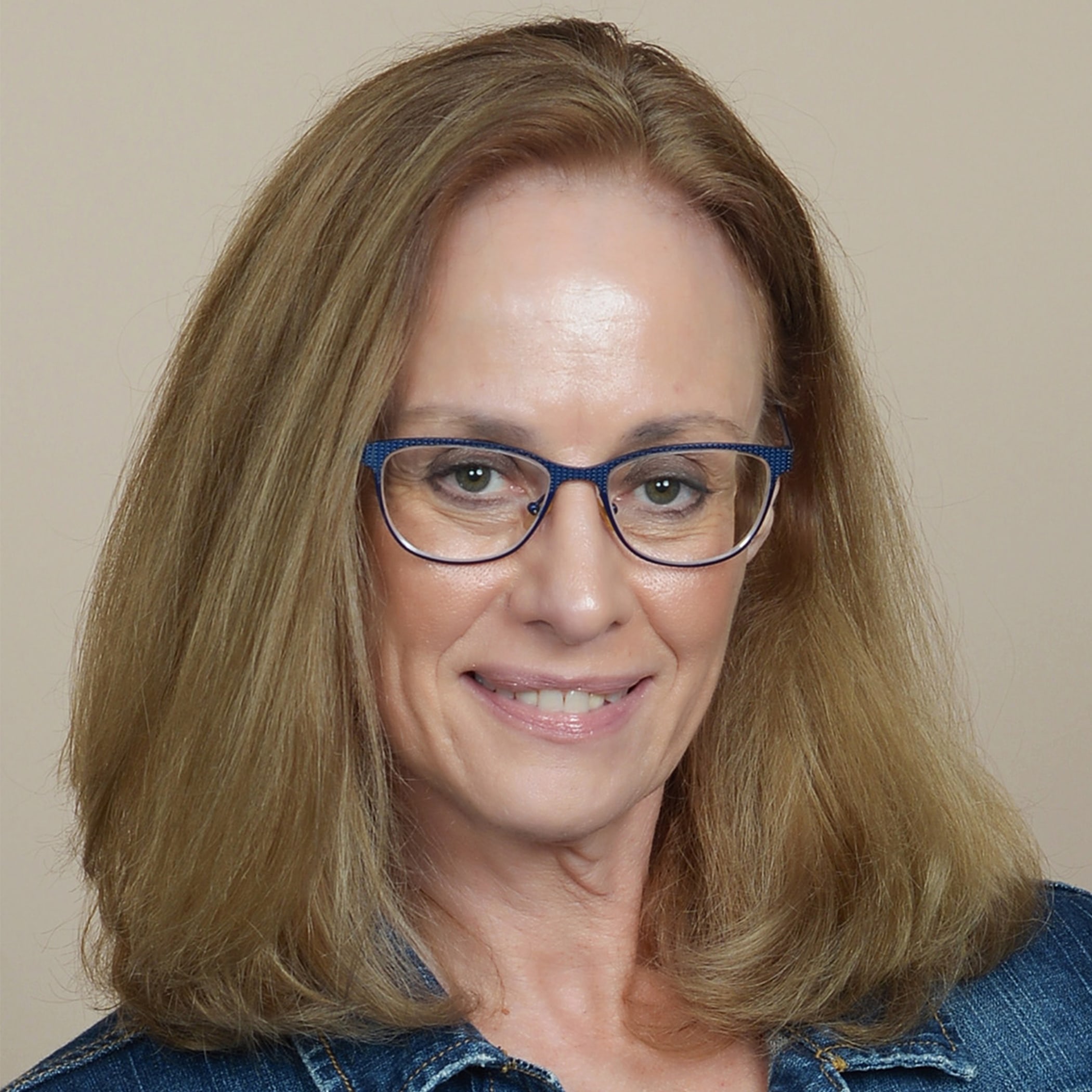 Karen Brooker headshot, brown hair, blue glasses, jean jacket