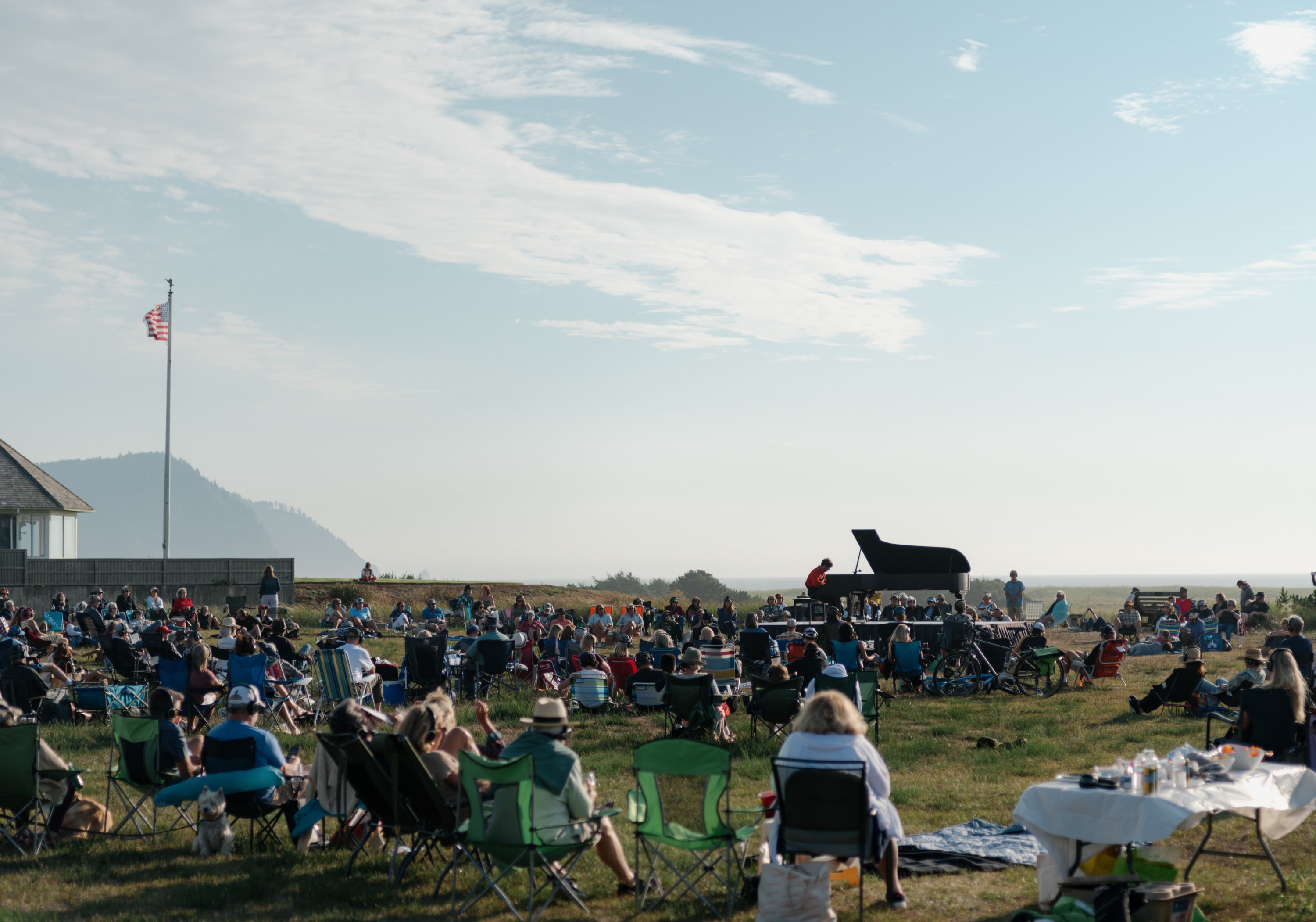 Hunter Noack sits at a piano surrounded by audience who members are seated in camp chairs watching Hunter play.  There is a f