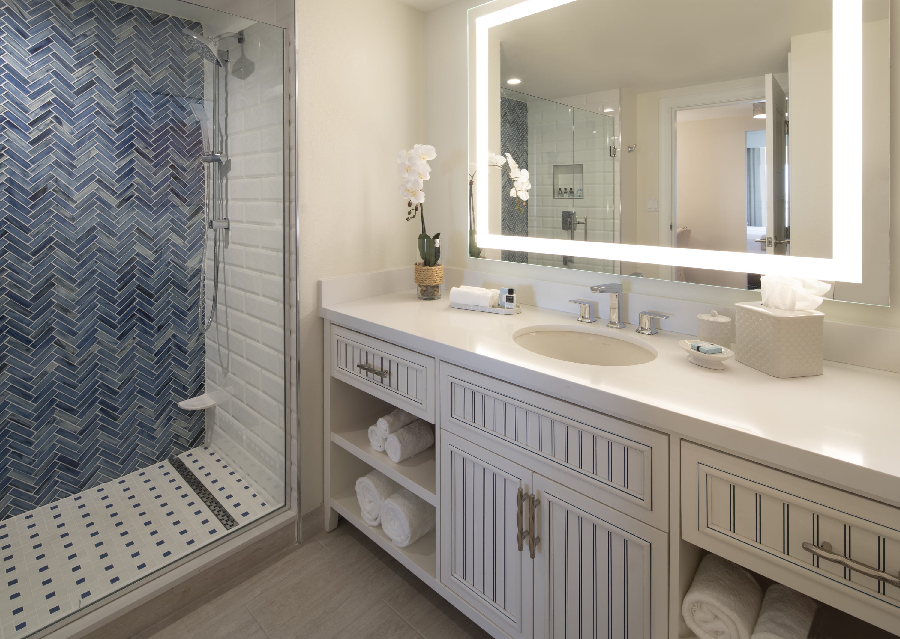 Bathromm with sink and large mirror and blue herringbone tiled shower with glass doors