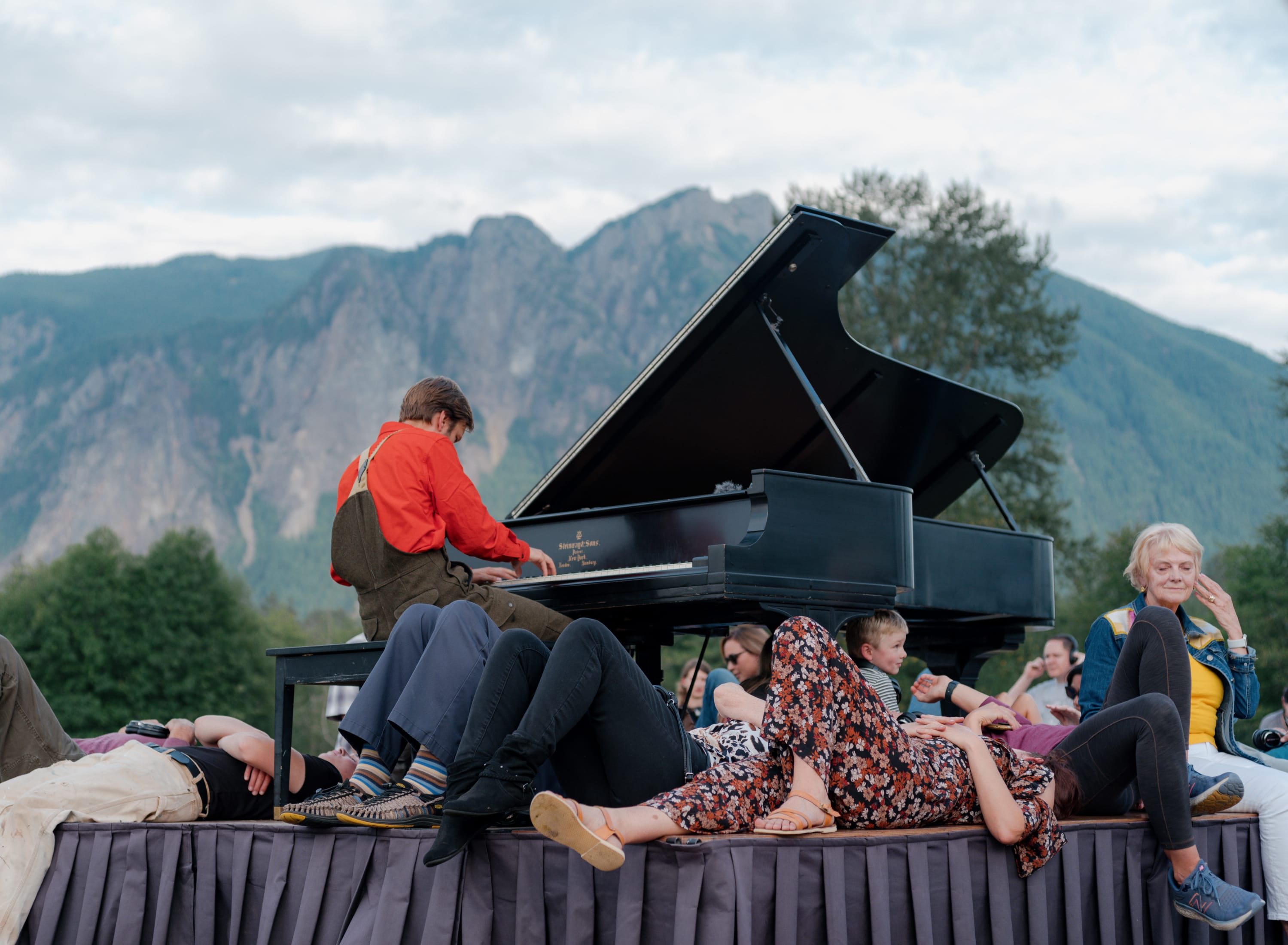 Hunter Noack is playing a piano on a trailer.  Audience members are sitting next to and under the piano listening.