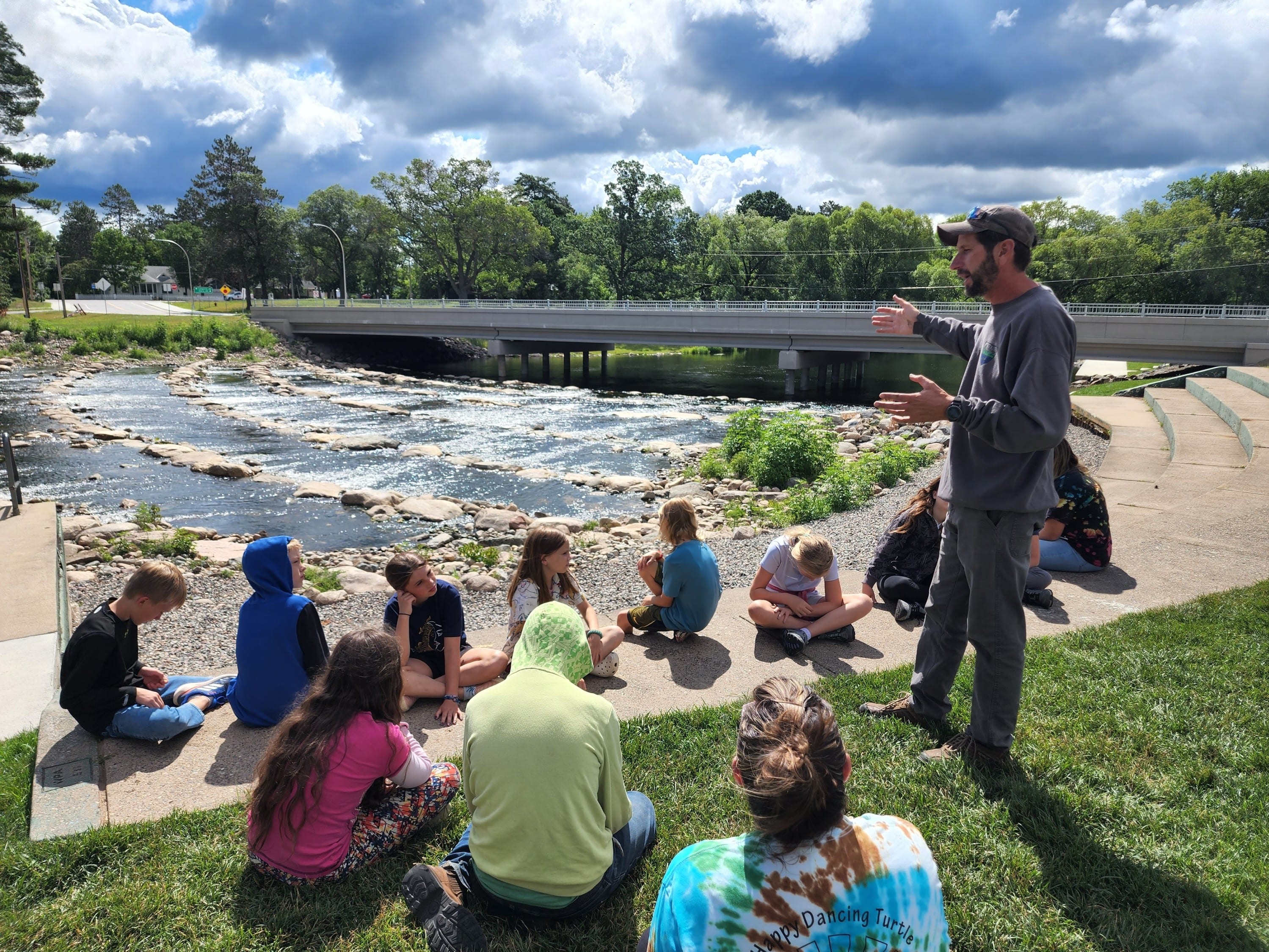 Kids listening to man speaking near river dam