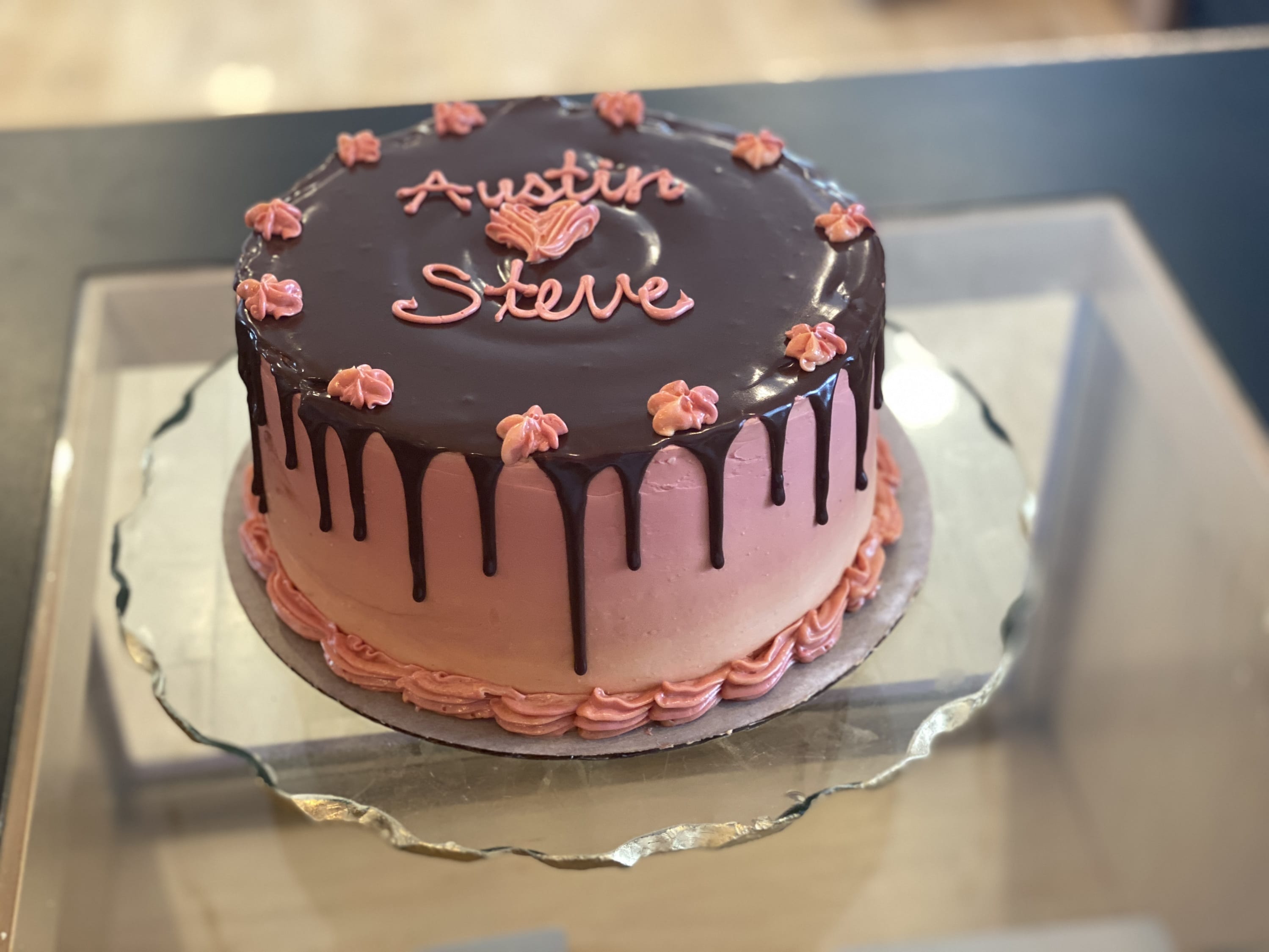 a peach and pink cake with a chocolate drip. The cake is inscribed with "Austin heart emoji Steve"