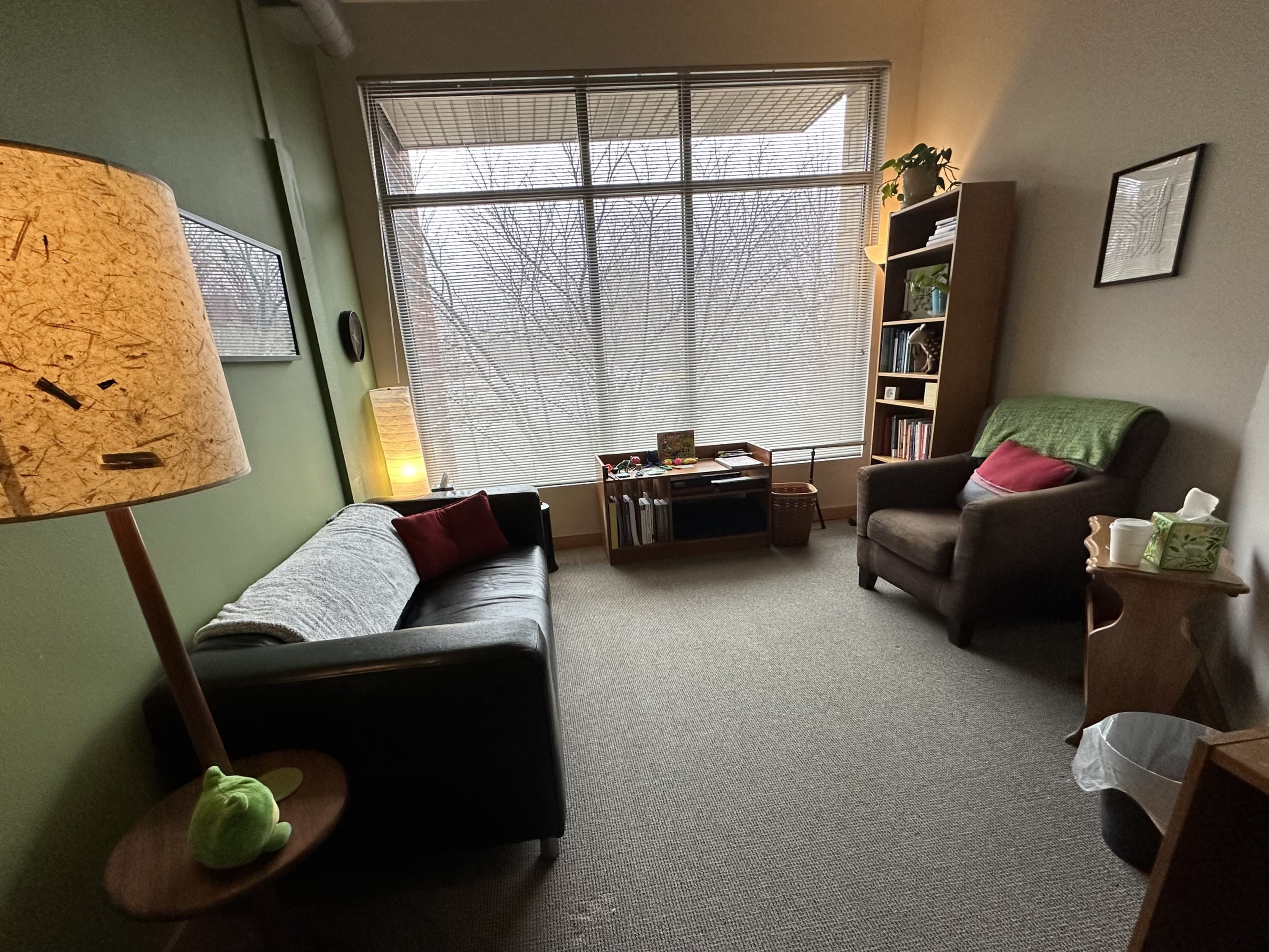 A photo of an office with a large window, a couch, a chair, and multiple lamps with warm lighting.