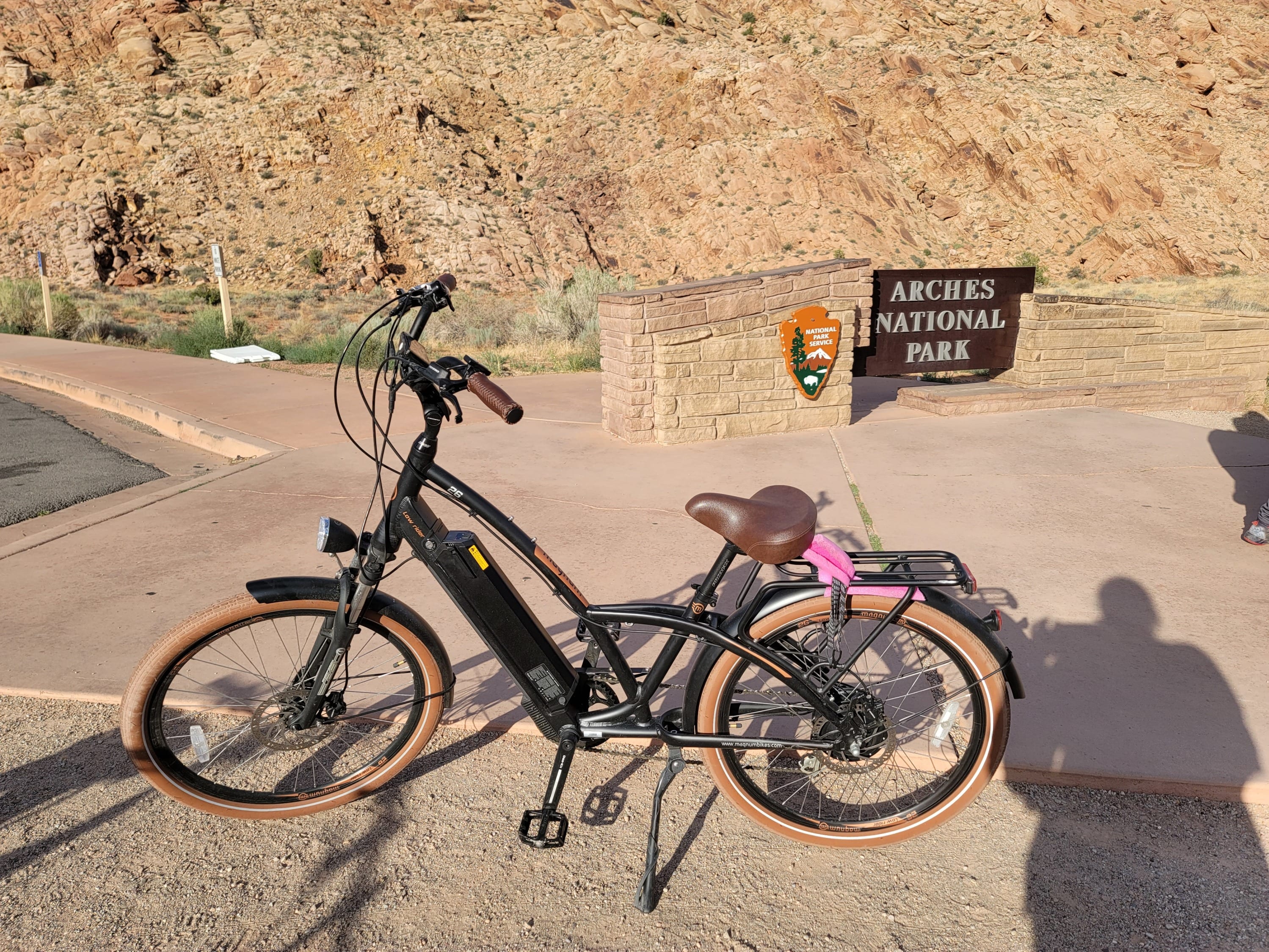 Electric bike parked at Arches National Park entrance sign with sandstone formations in the background
