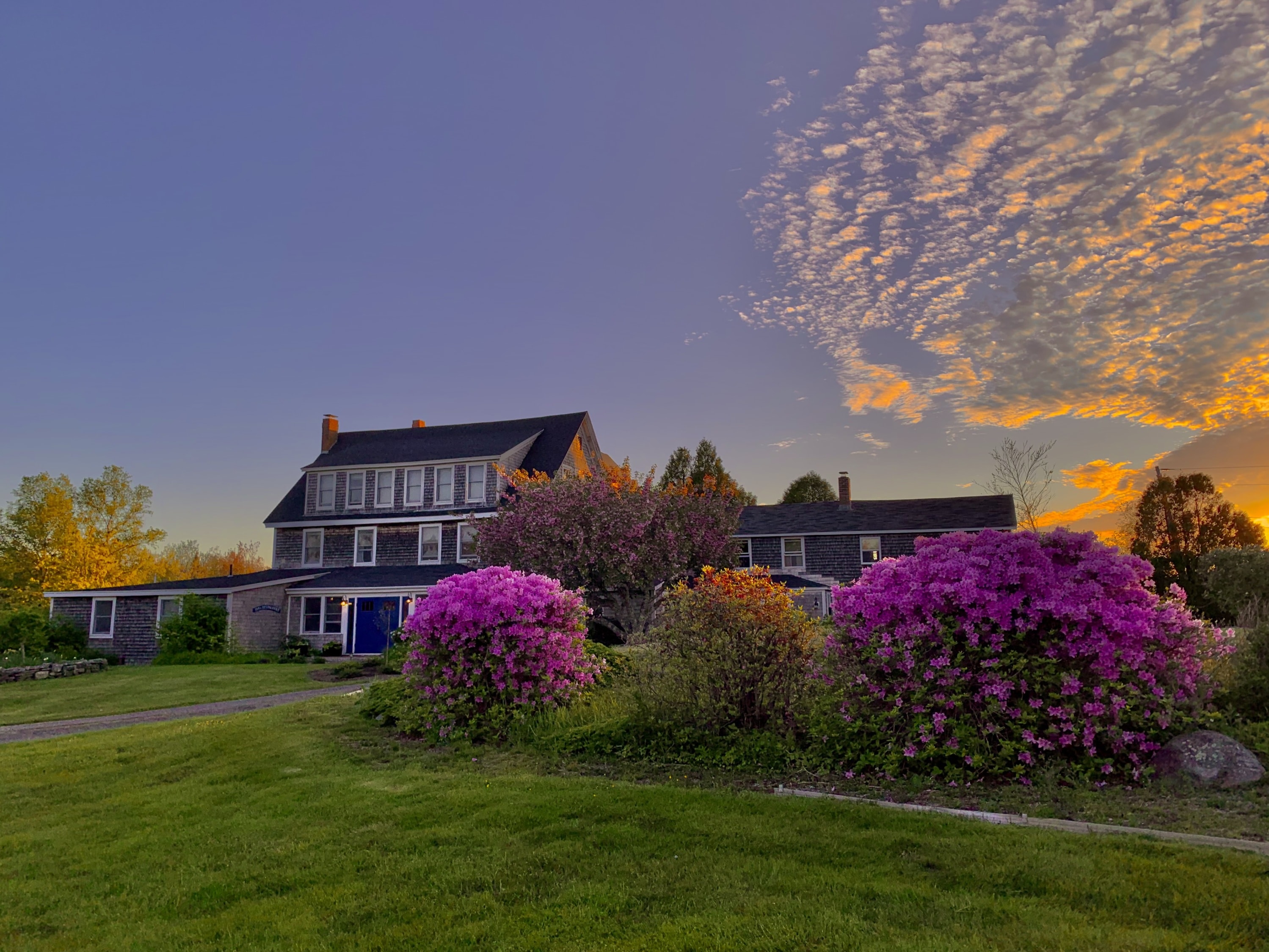 Sunset photo of the Bradley Inn with orange clouds.  Hot pink azaleas are blooming in the foreground.