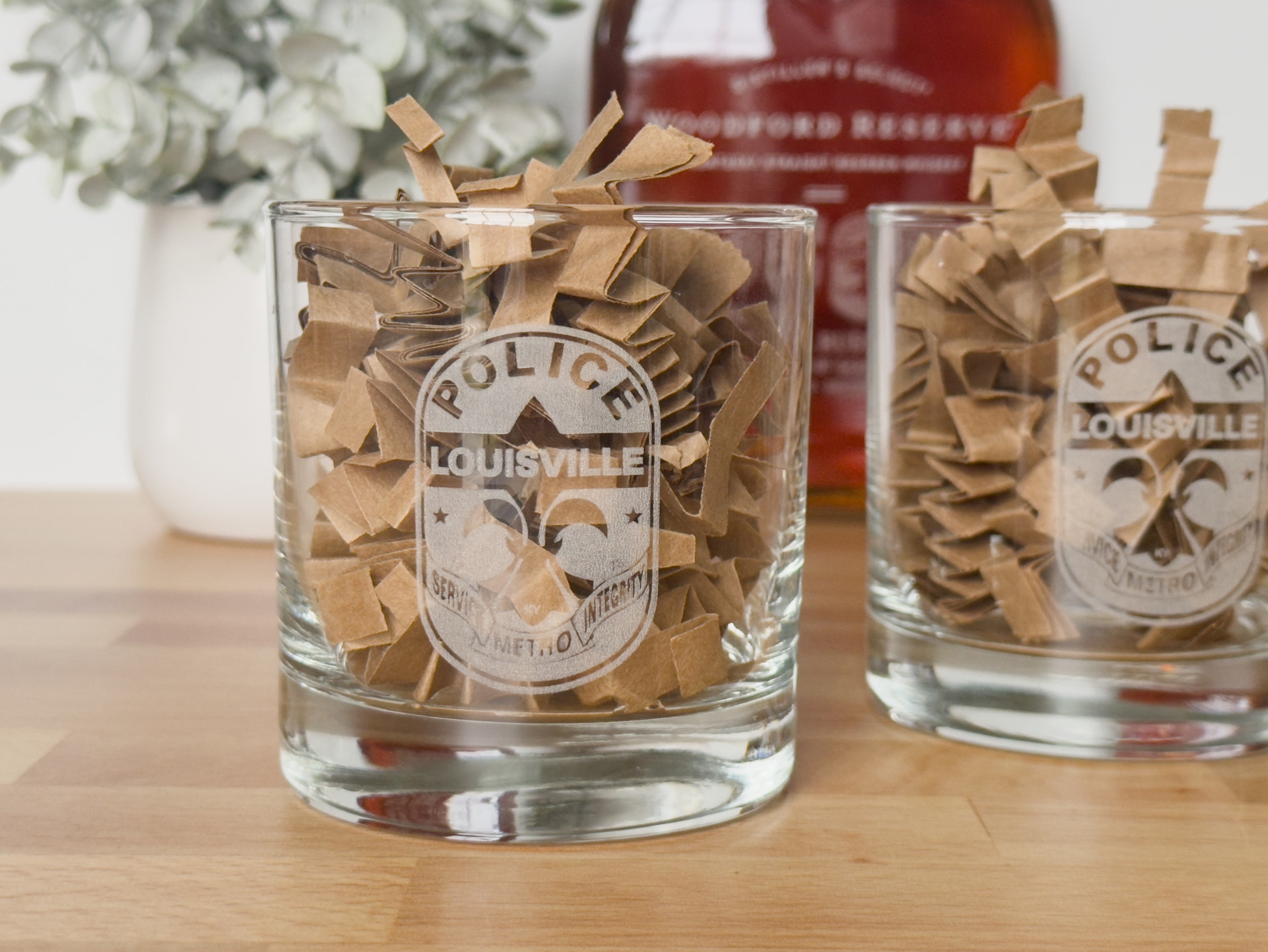 engraved/etched bourbon glasses with the LMPD logo and a bottle of Woodford reserve in the background