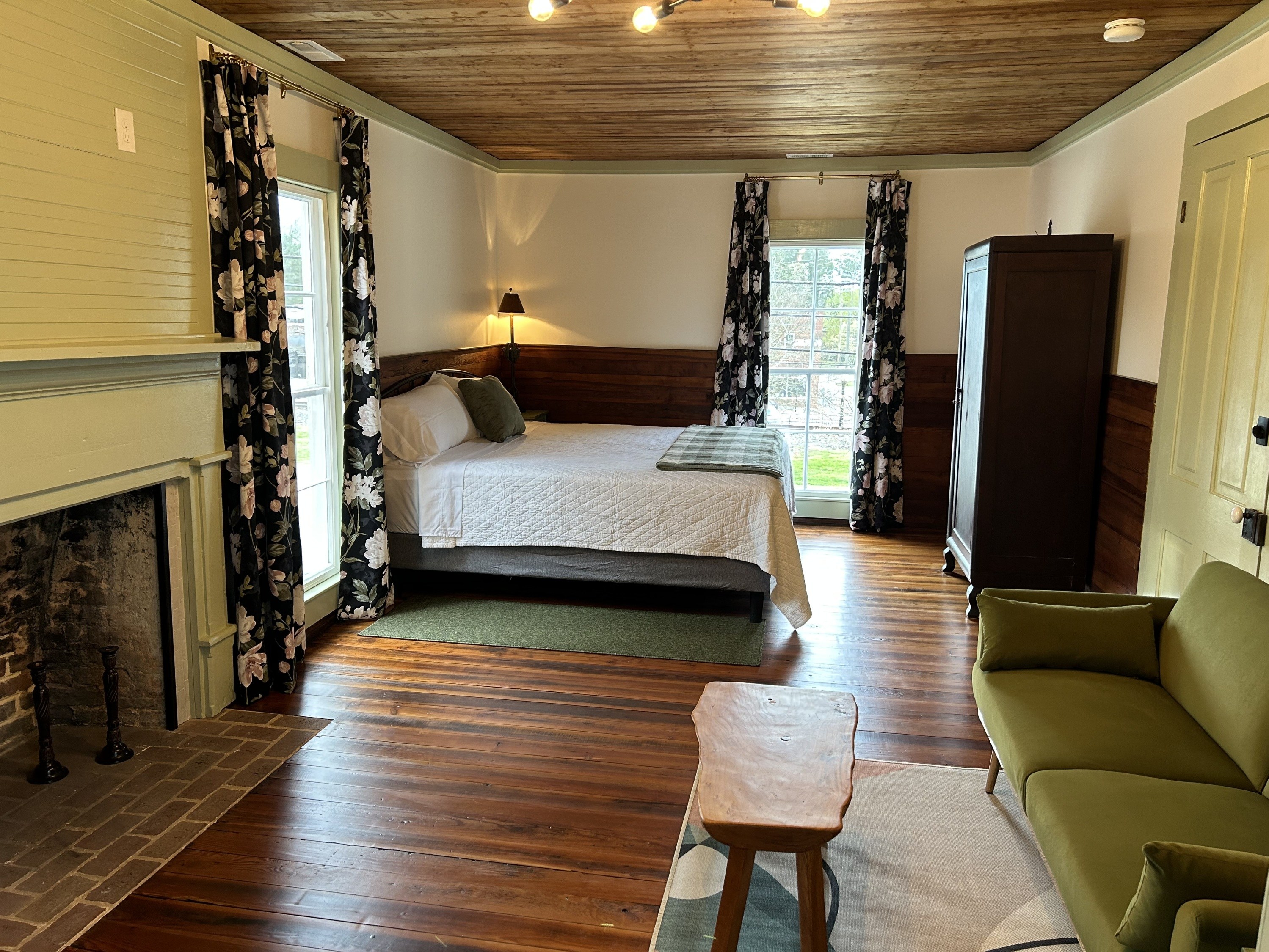 Room with wooden floor, green couch, bed, and cabinet. Fireplace on left.