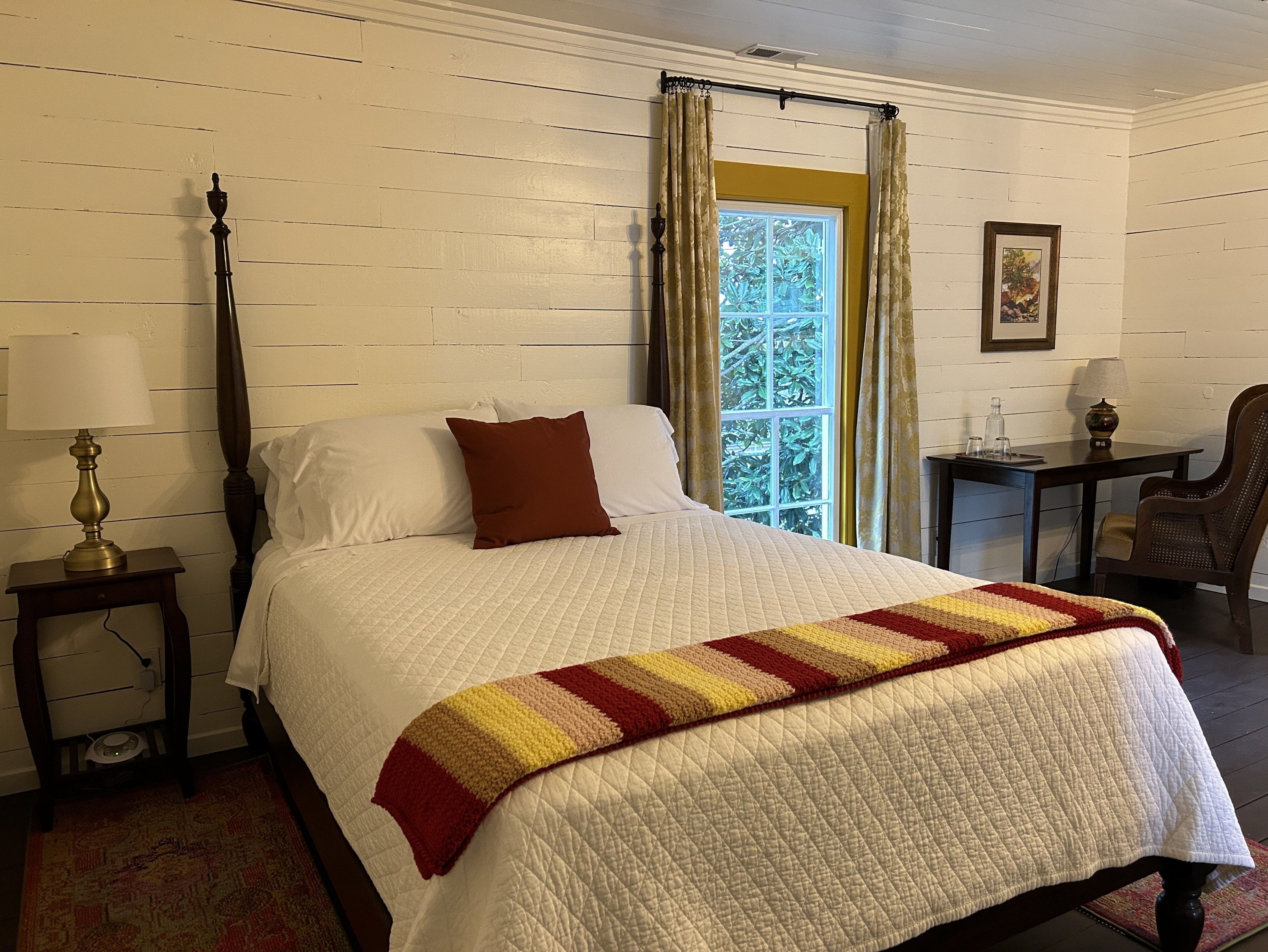 White bedspread on bed with colored comforter and red pillow.