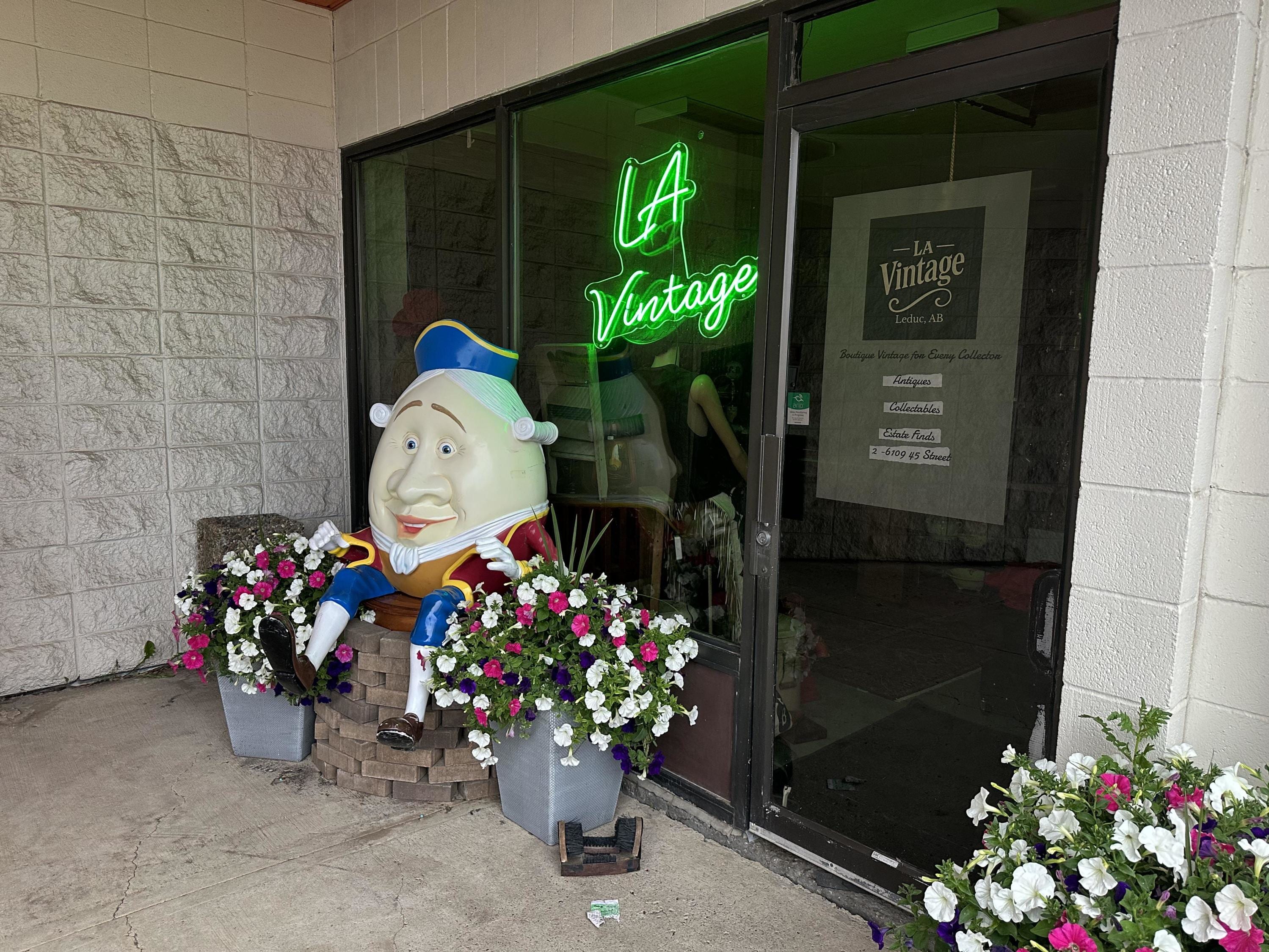 LA Vintage storefront in Leduc with neon sign, Humpty Dumpty statue, and flower planters.