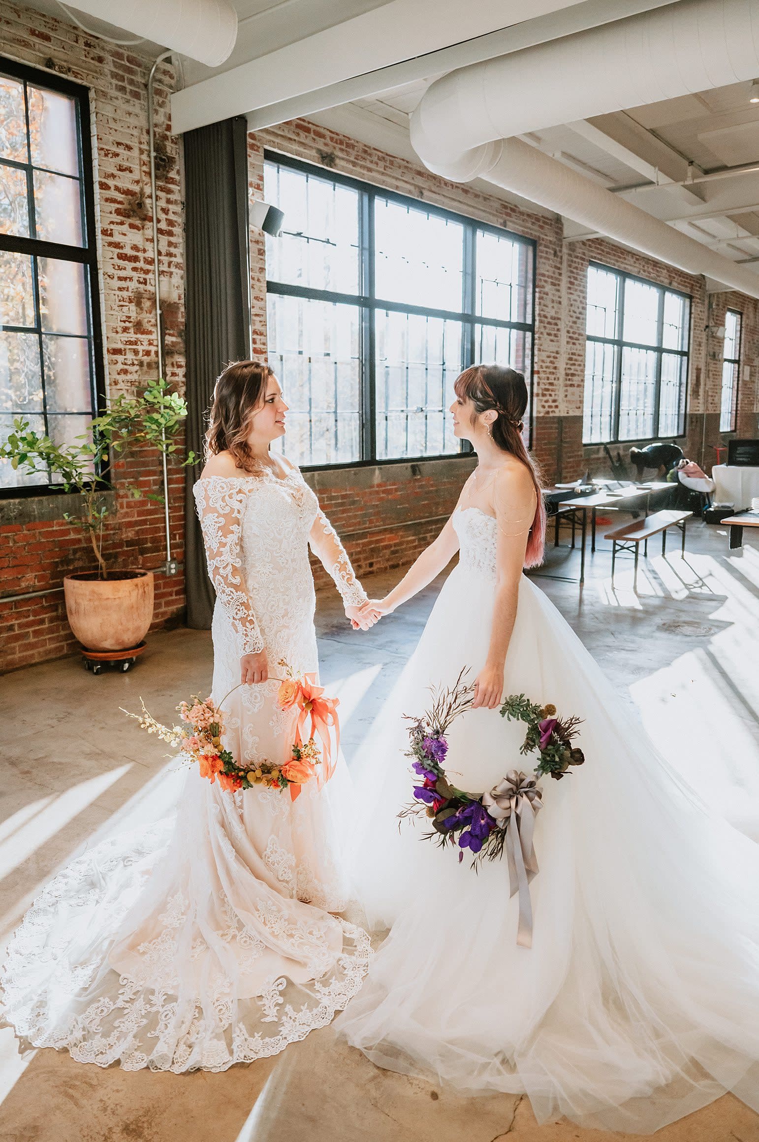Two Brides hold hands in their wedding dresses on their wedding day with their wedding flower circles