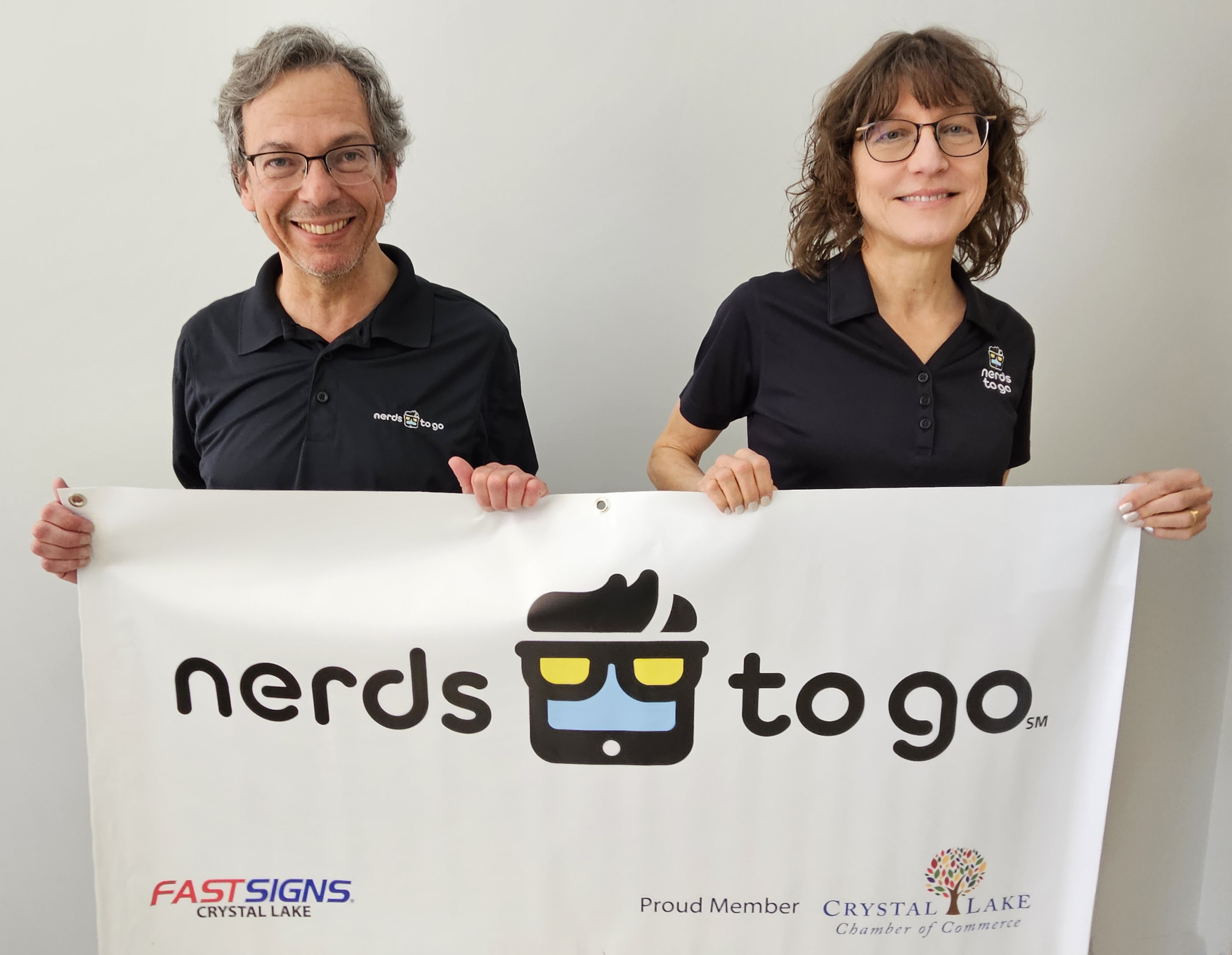 A man and a woman wearing glasses hold a Nerds to Go banner
