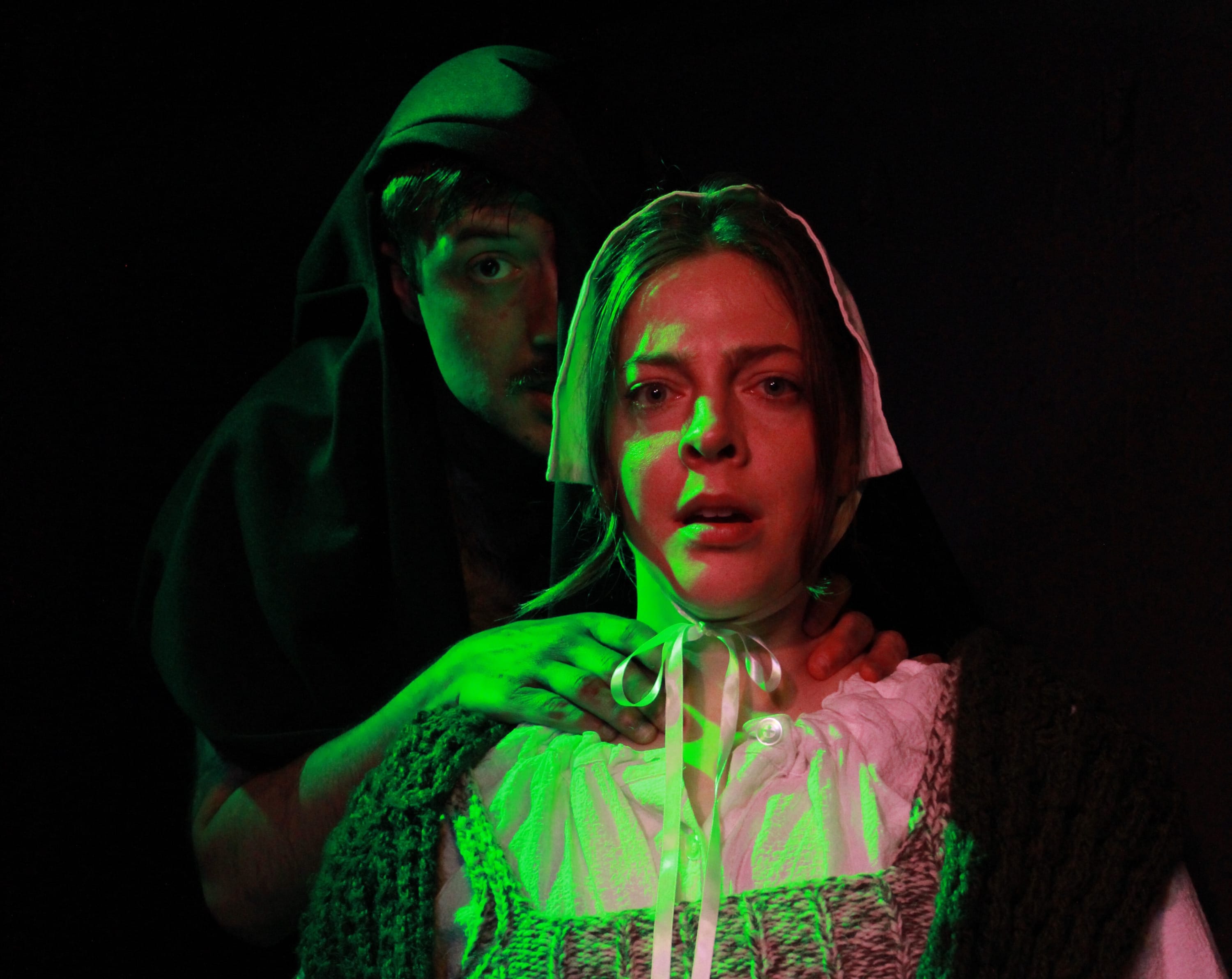 Shadowy figure in a cloak reaching threateningly towards a scared woman in a bonnet, both bathed in green light