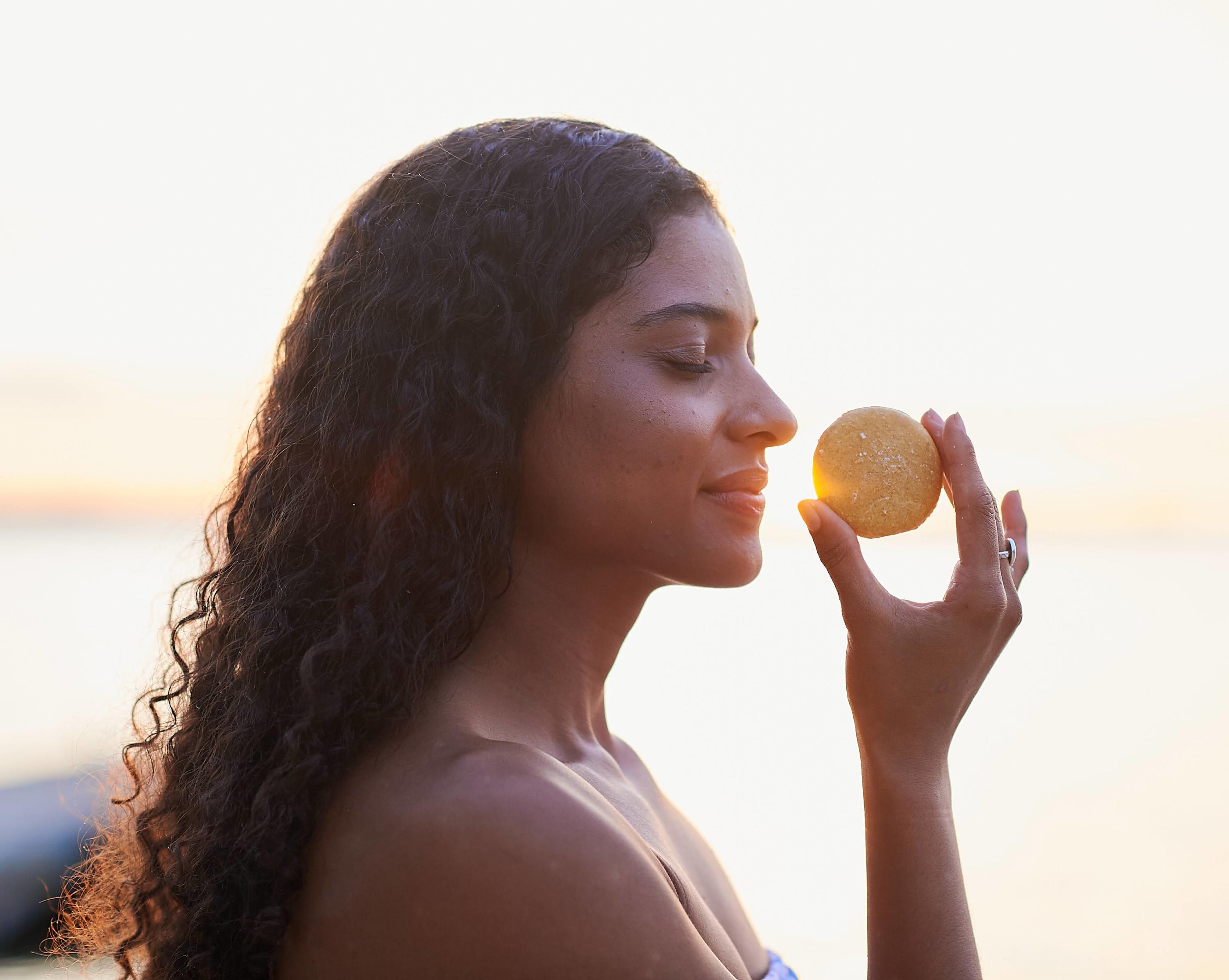 Woman smelling a Tangie plastic-free shampoo bar at sunset, a natural zero-waste hair care alternative to bottled shampoo.