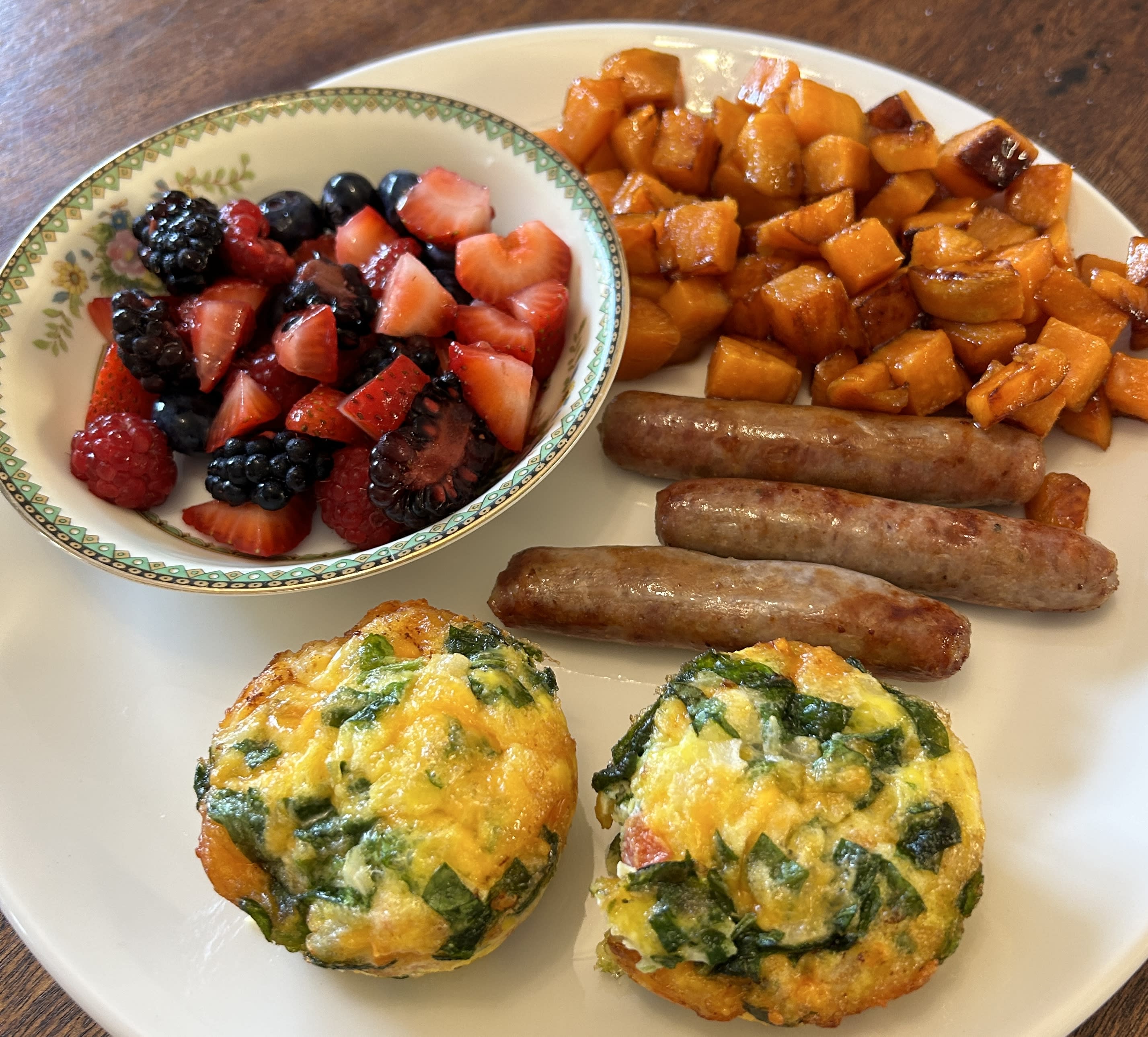 Breakfast plate with egg puffs, sausages, sweet potatos, and mixed fruit.
