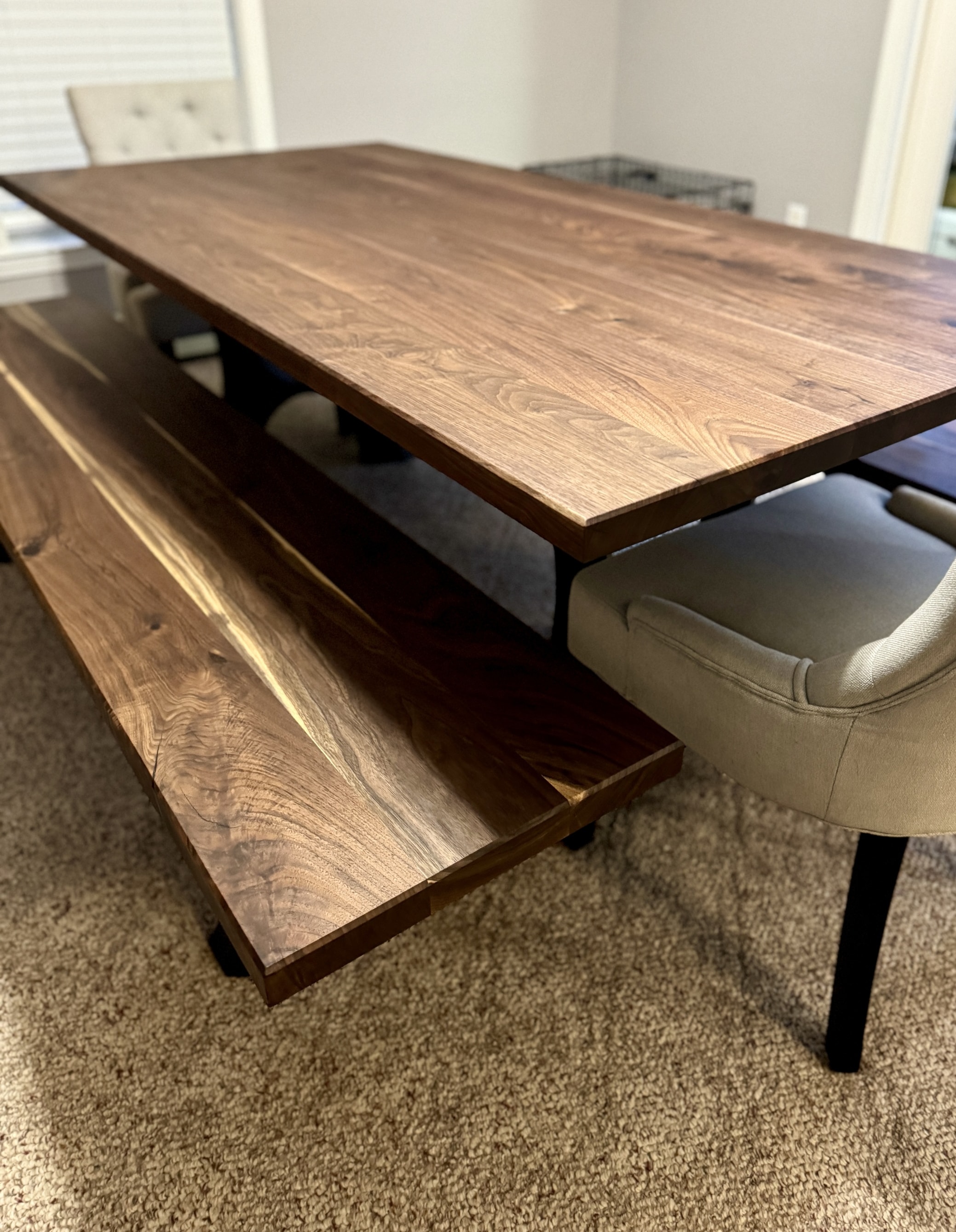 A close-up view of a modern dining set featuring a large, rectangular walnut wood dining table and a matching walnut bench
