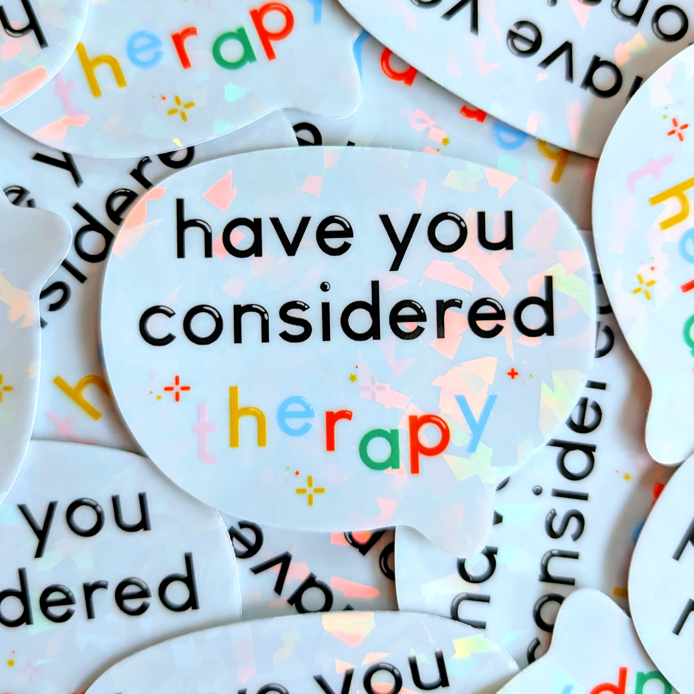 Holographic sticker that's in the shape of a speech bubble and says "have you considered therapy"