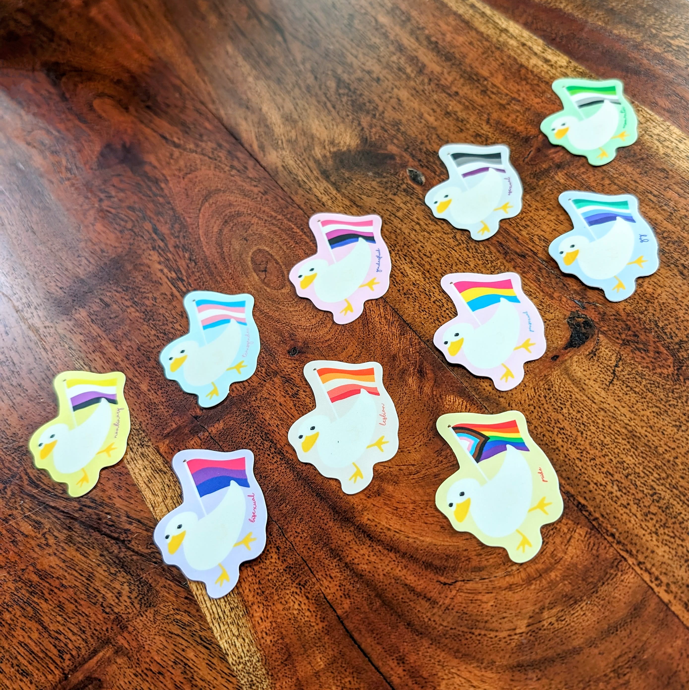 Eleven stickers of ducks holding pride flags.