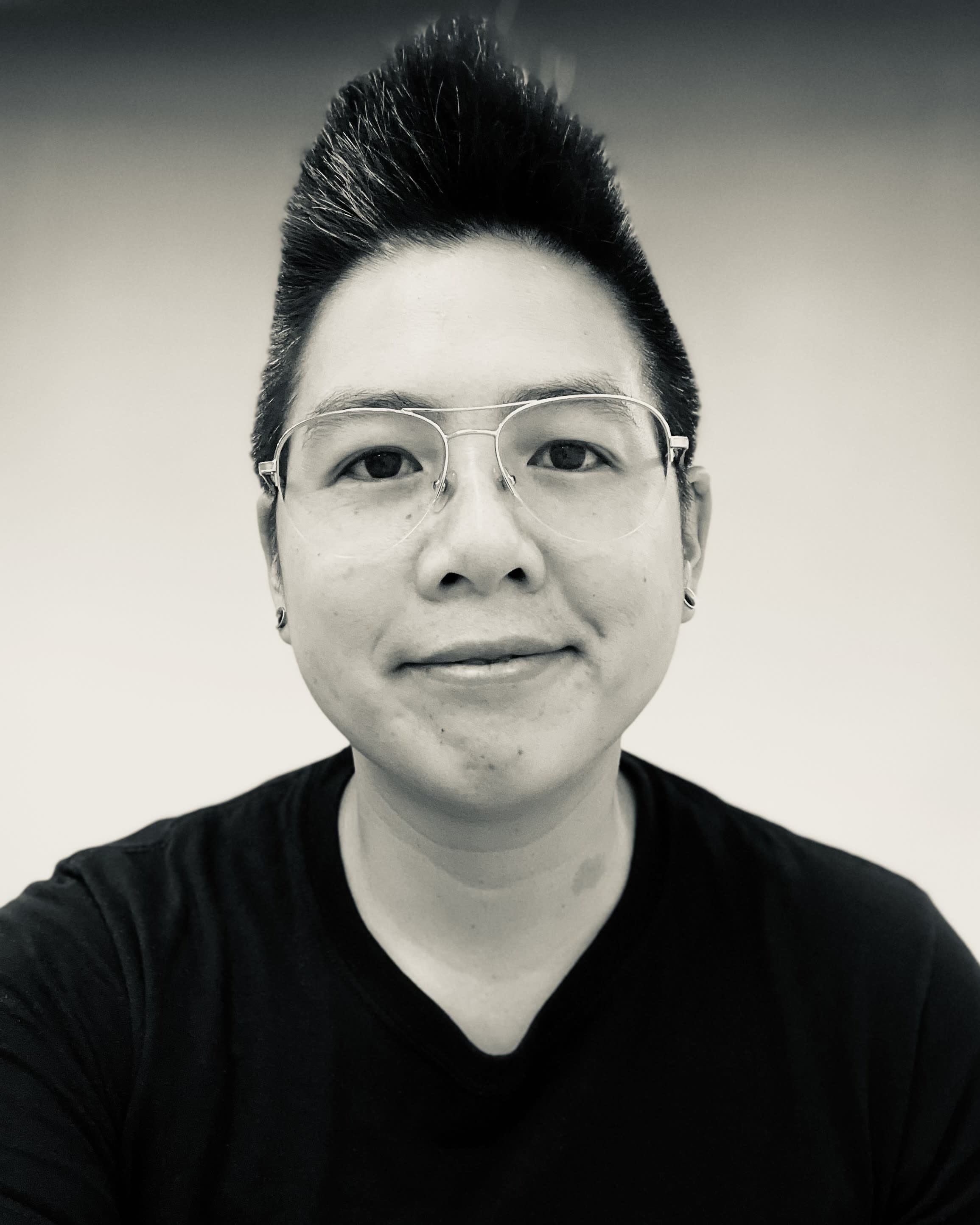 A headshot of a Chinese American woman with very short, stylish hair, a black t shirt, and wire-framed glasses
