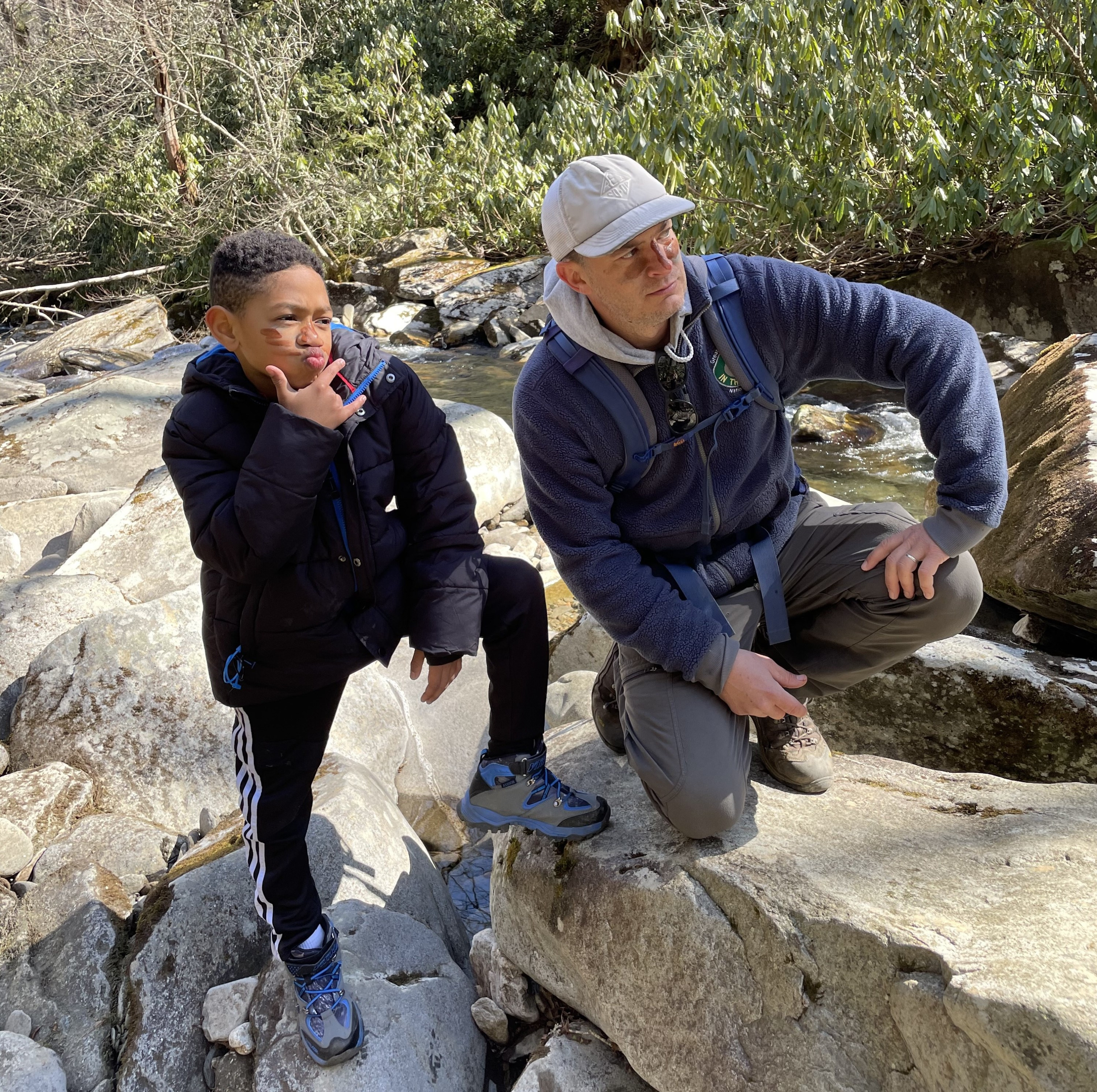 Trail guide and kid pose for a photo on rocks in a mountain stream