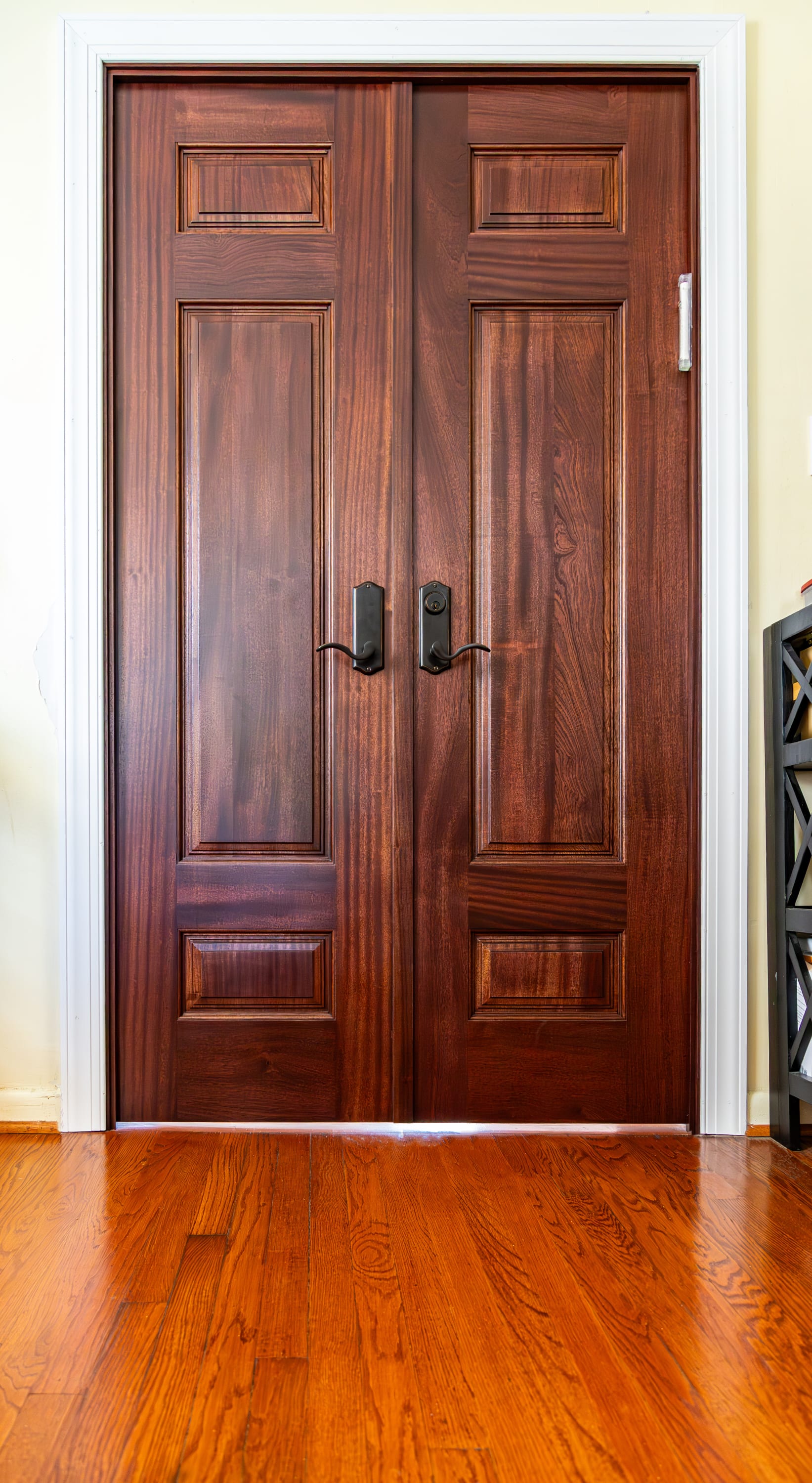 A pair of rich, dark sapele wood interior double doors with three raised panels on each door