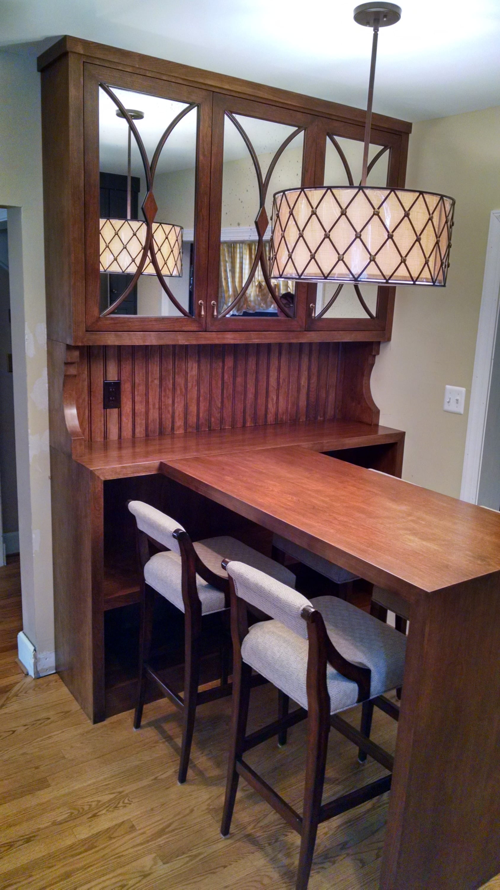 A custom dark wood home bar or hutch unit featuring upper mirrored cabinets with decorative grilles