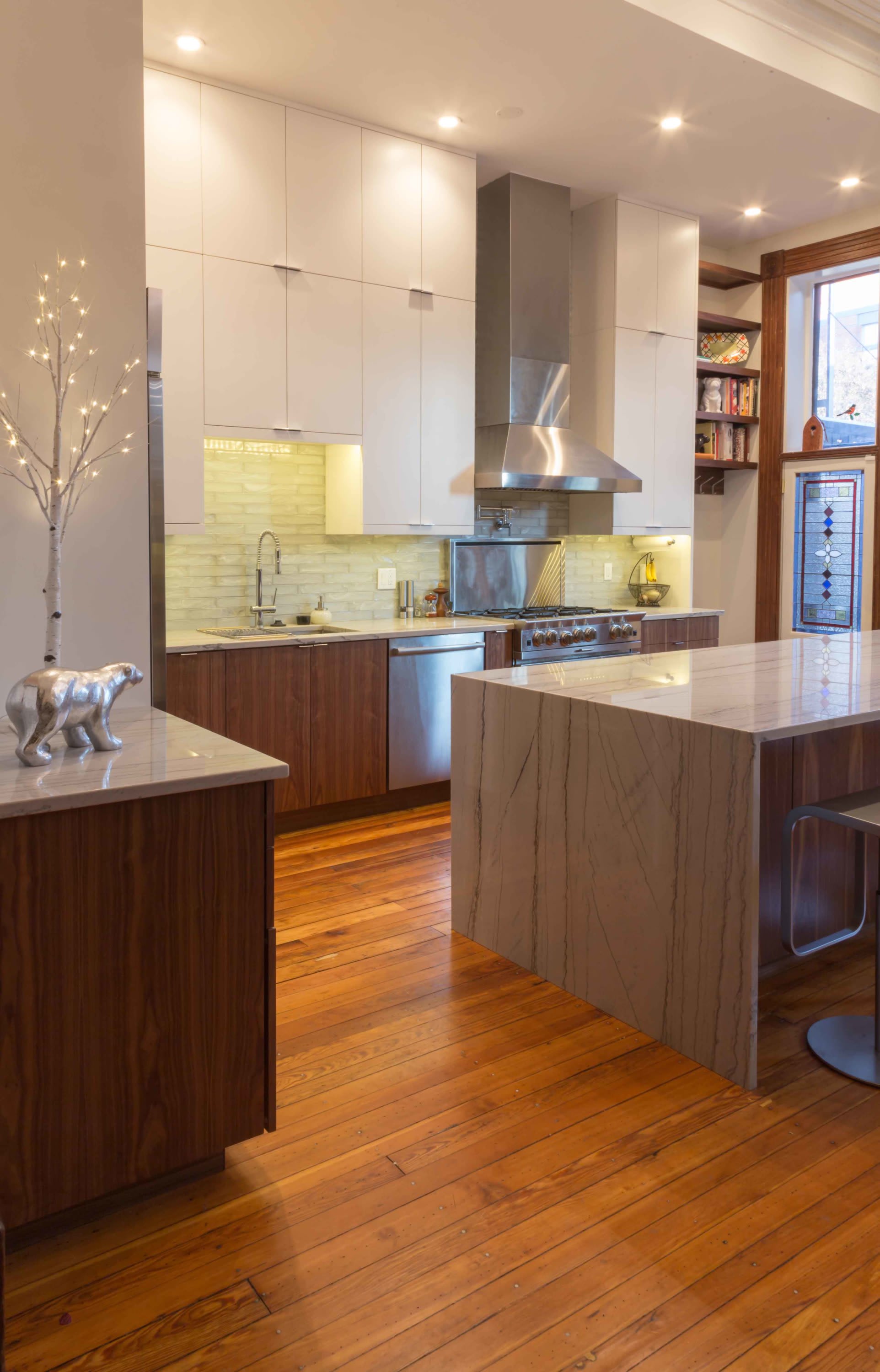 Modern kitchen with custom two-tone cabinetry, quartz waterfall island, stainless steel appliances, and warm wood flooring.