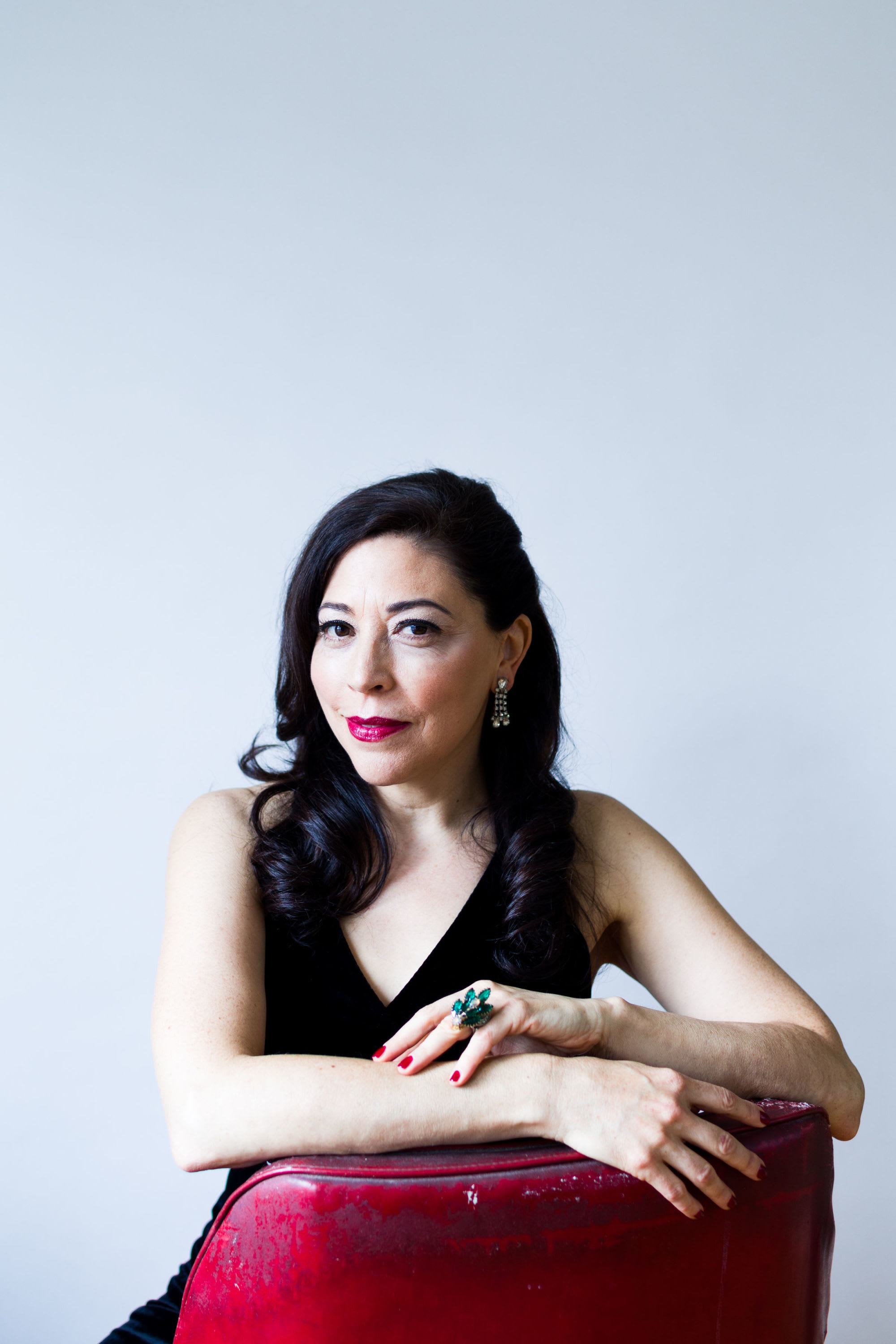 Tina D'Elia in a black dress sitting in a red leather chair