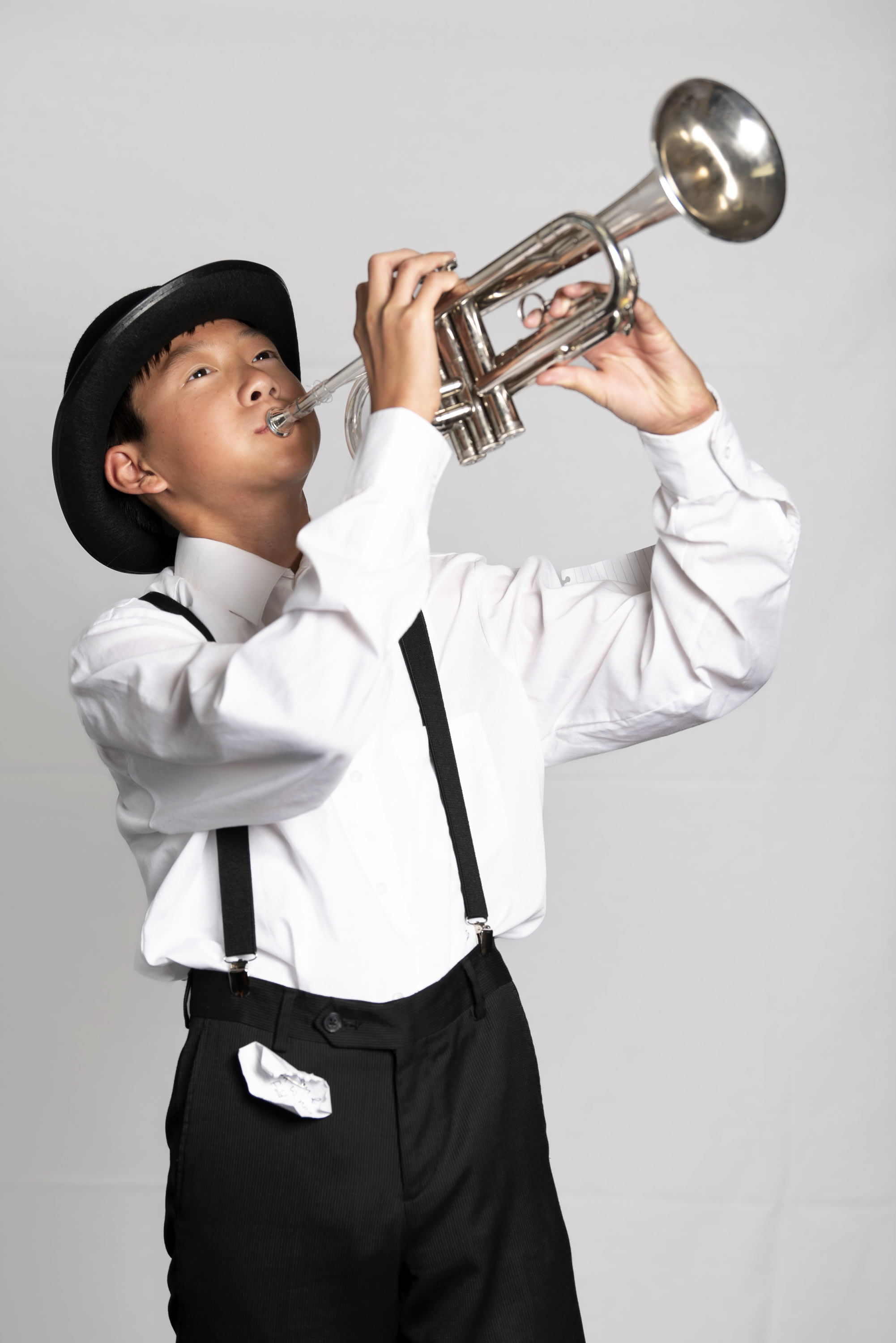 Chicago cast member in a white button down shirt, black pants and suspenders playing the trumpet