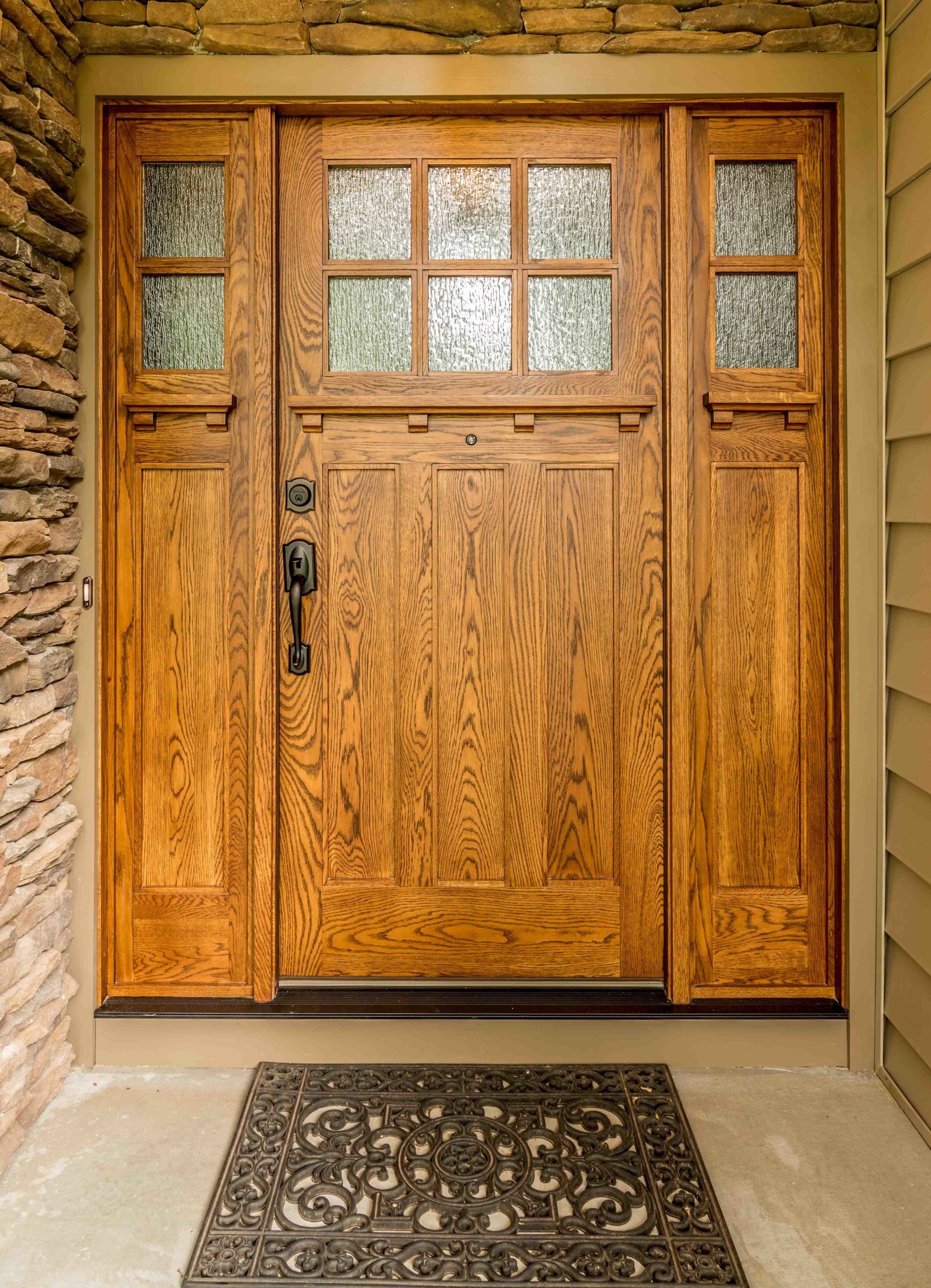 Custom solid oak entry door with sidelights and decorative glass panels, handcrafted with vertical grain detailing