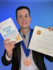 Rick Joi wearing medal, and holding both Inspiring Work Anniversaries and an Axiom Business Book Awards award certificate