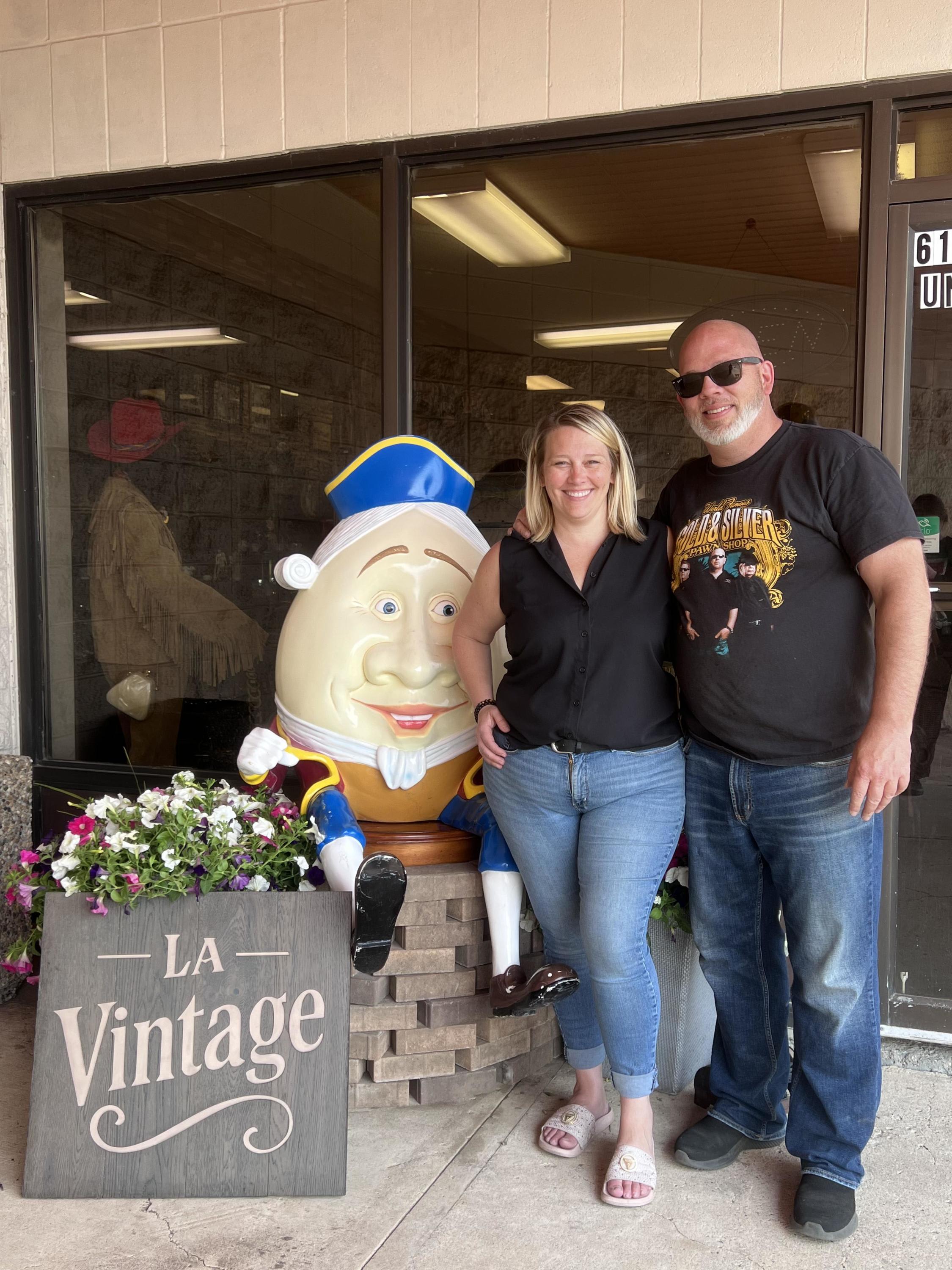Michelle and Spencer, owners of LA Vintage in Leduc, standing outside the shop beside Humpty Dumpty and the store sign.