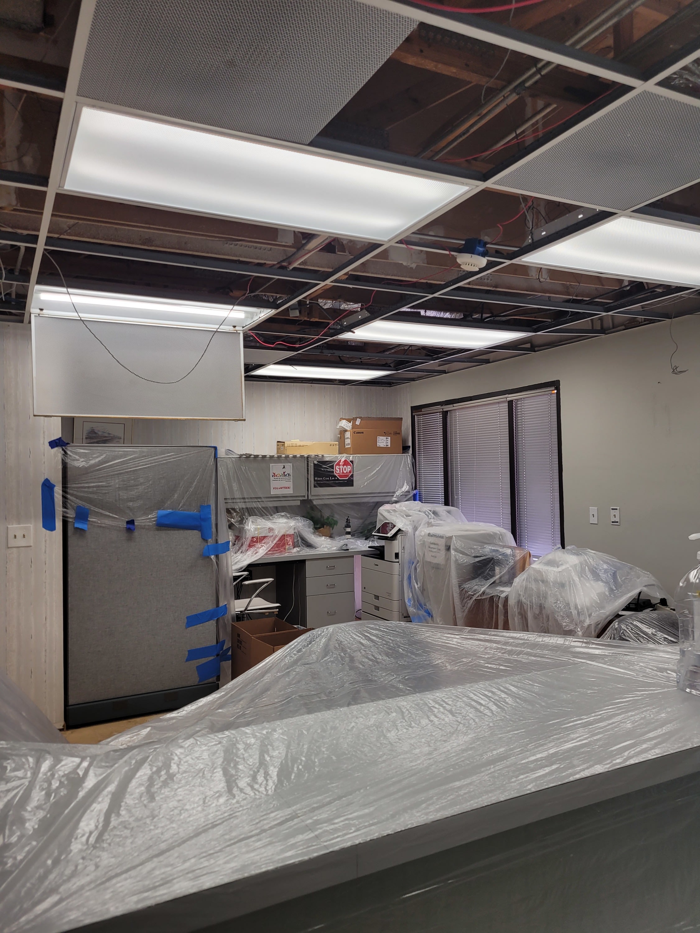 Image of the reception area with exposed ceilings and furniture and equipment covered in protective plastic sheeting