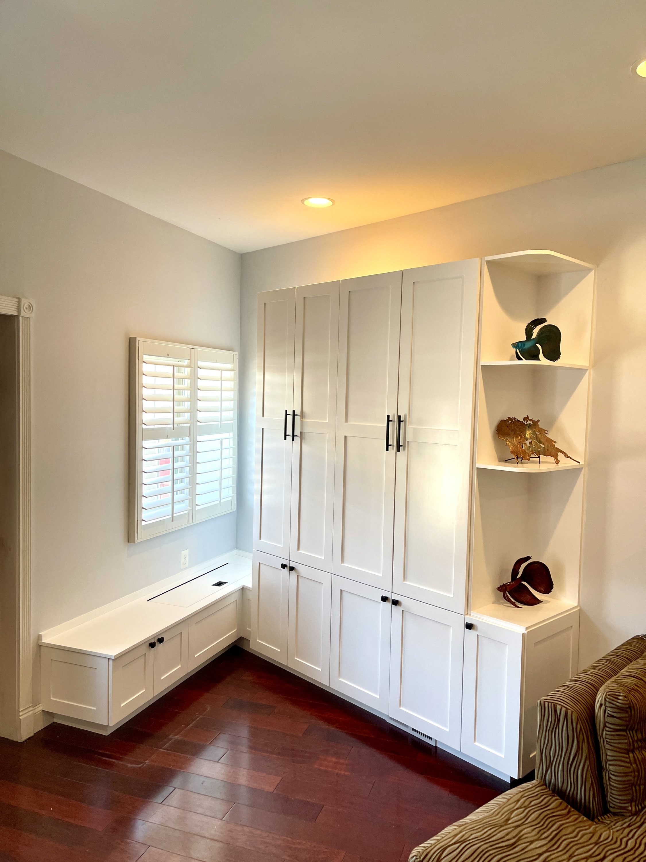 A corner of a room featuring custom white built-in cabinetry, including a window seat with storage, tall closed cabinets