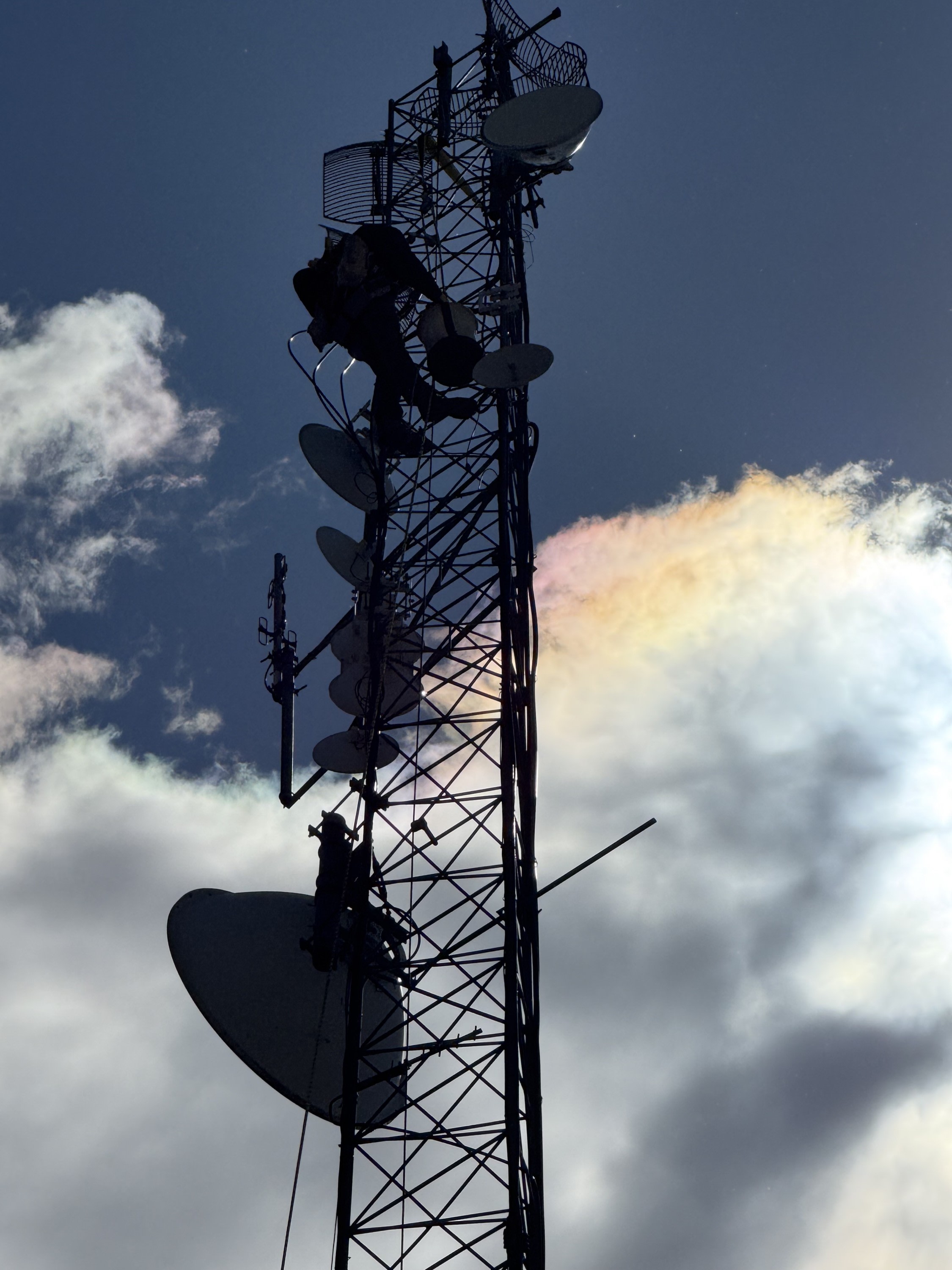 upward view of a person on a tower with satellites and a cloud in the background with a rainbow in it