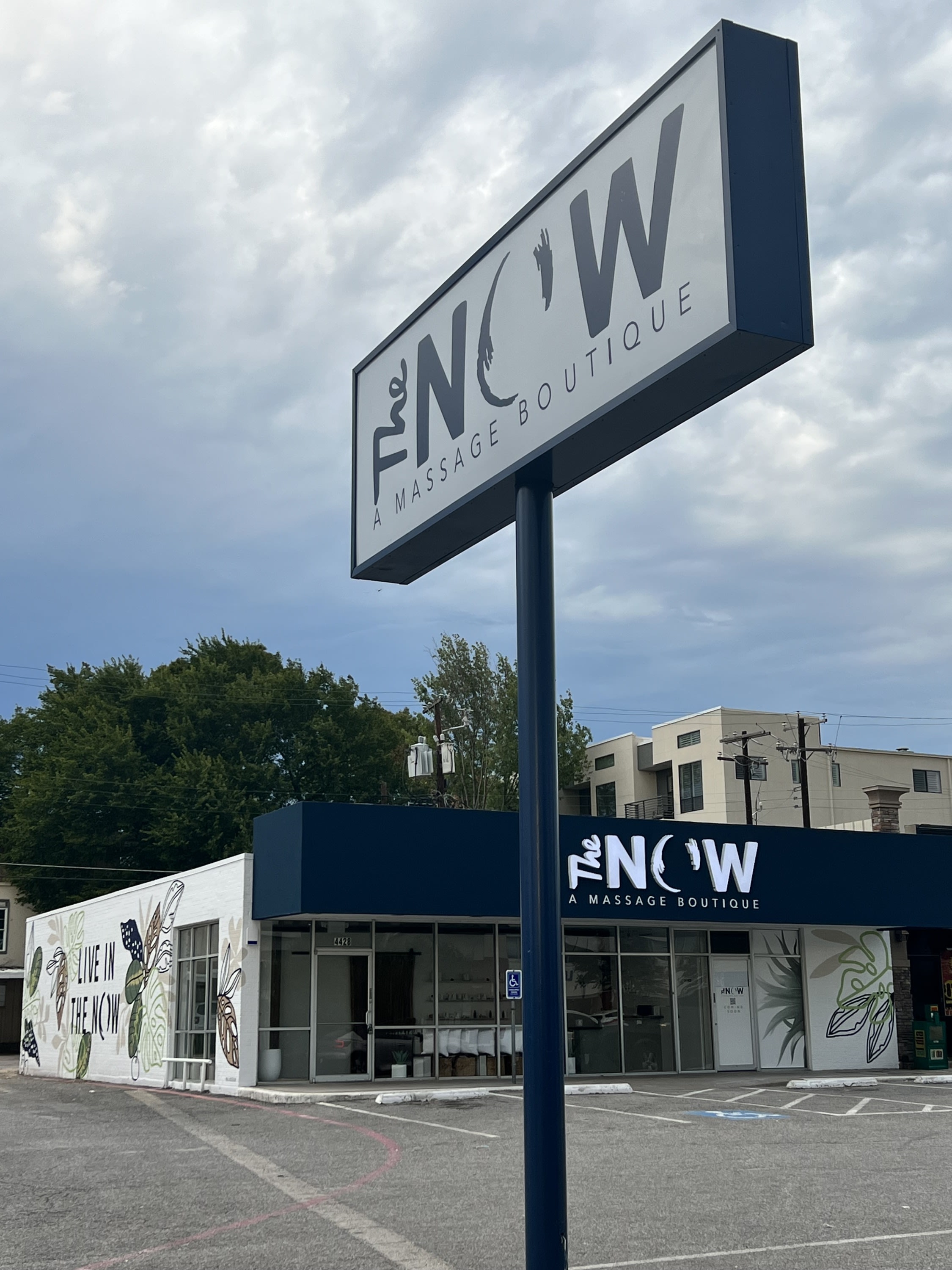 Exterior of The NOW Massage Oak Lawn Dallas with pylon sign and signature mural