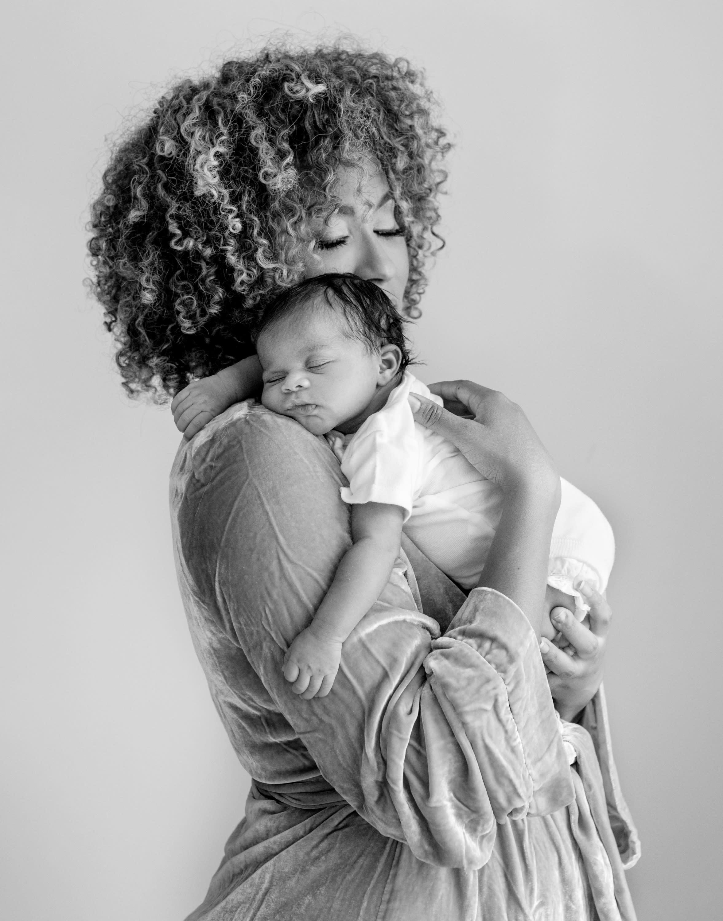 Black and white image of African American mother in robe tenderly holding newborn baby on her shoulder