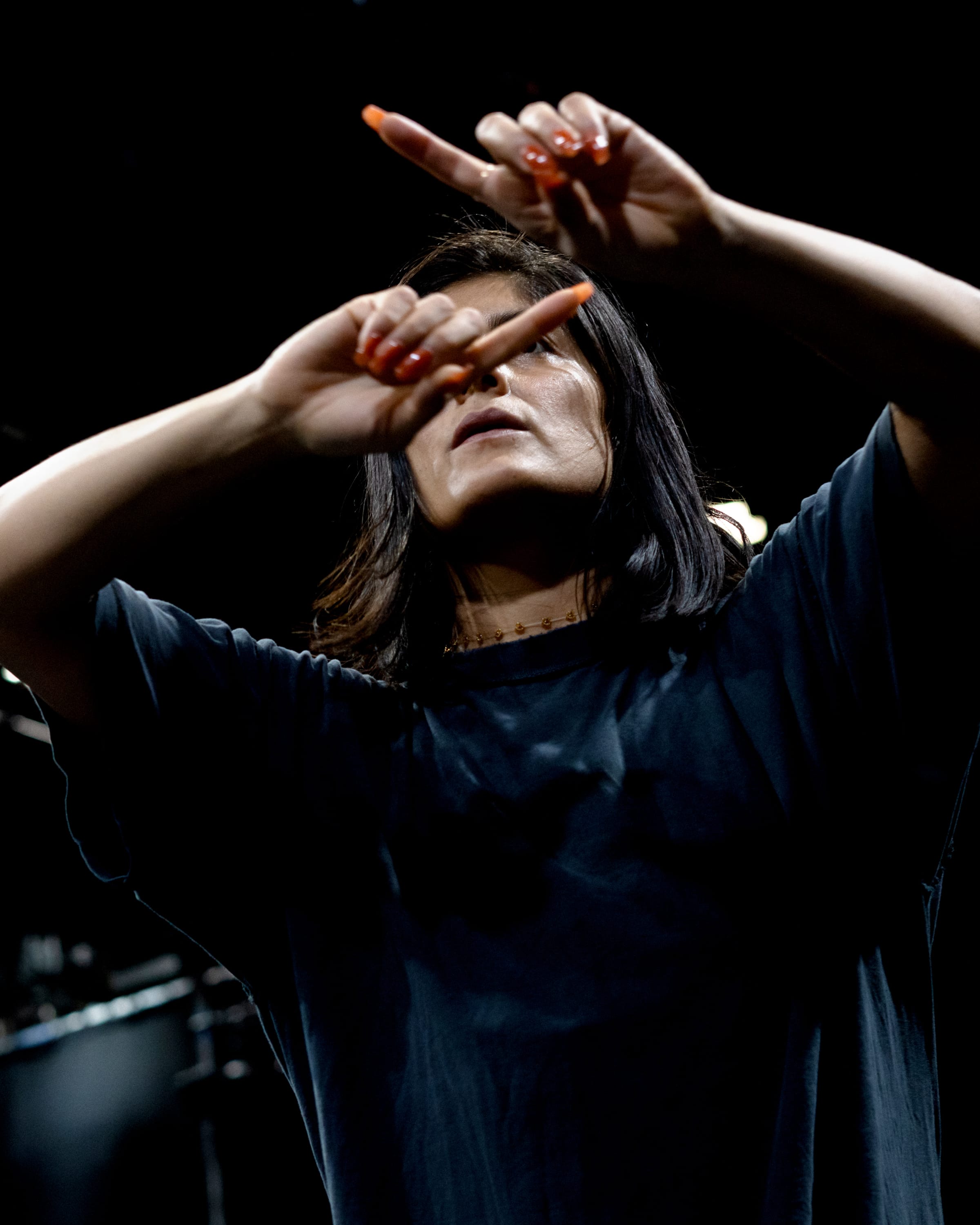 Dancer with long dark hair gestures above face with orange finger nails