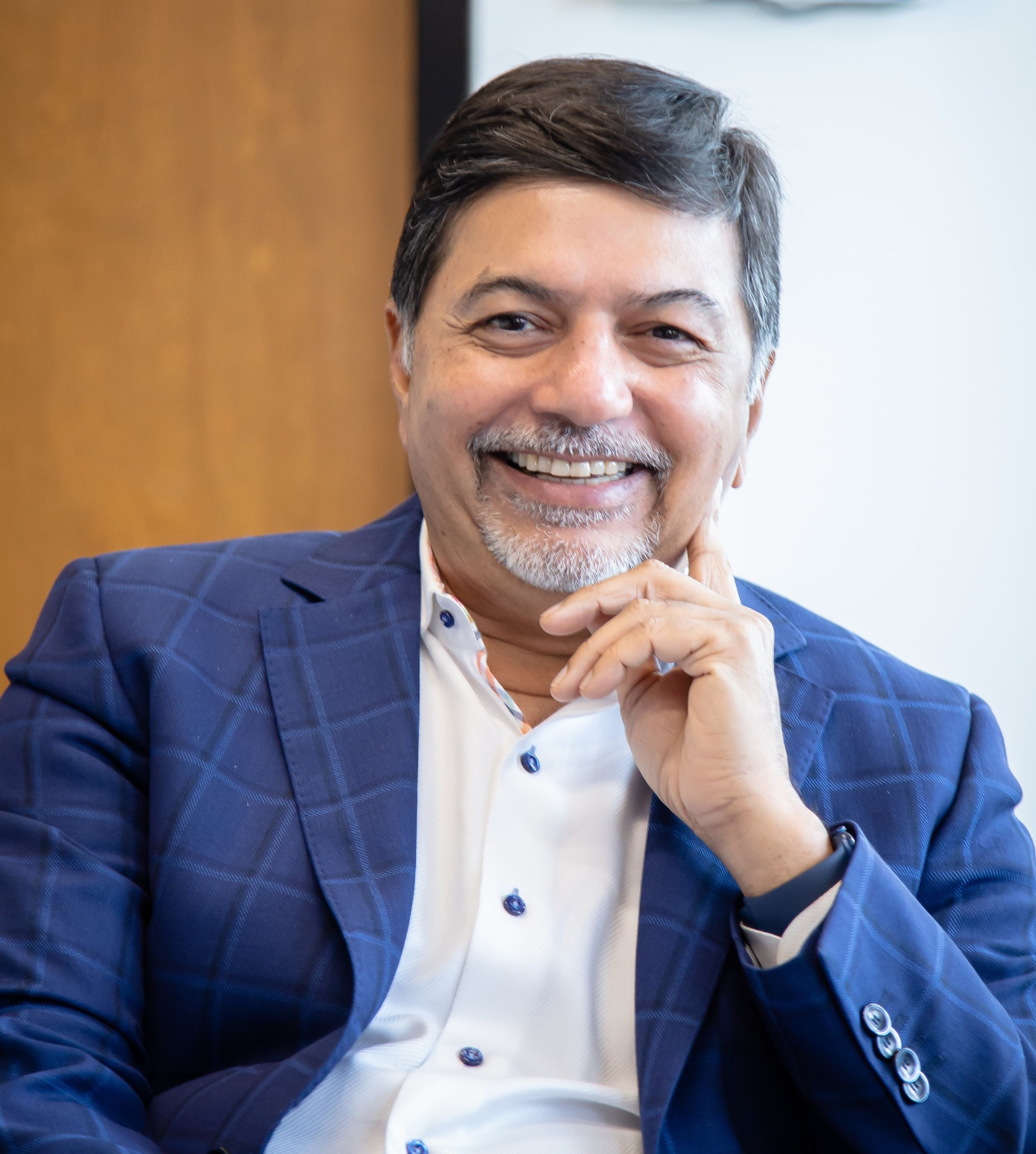 Headshot of Raj Sisodia, a middle-aged Indian man with greying hair and a light beard, smiling warmly and wearing a suit.