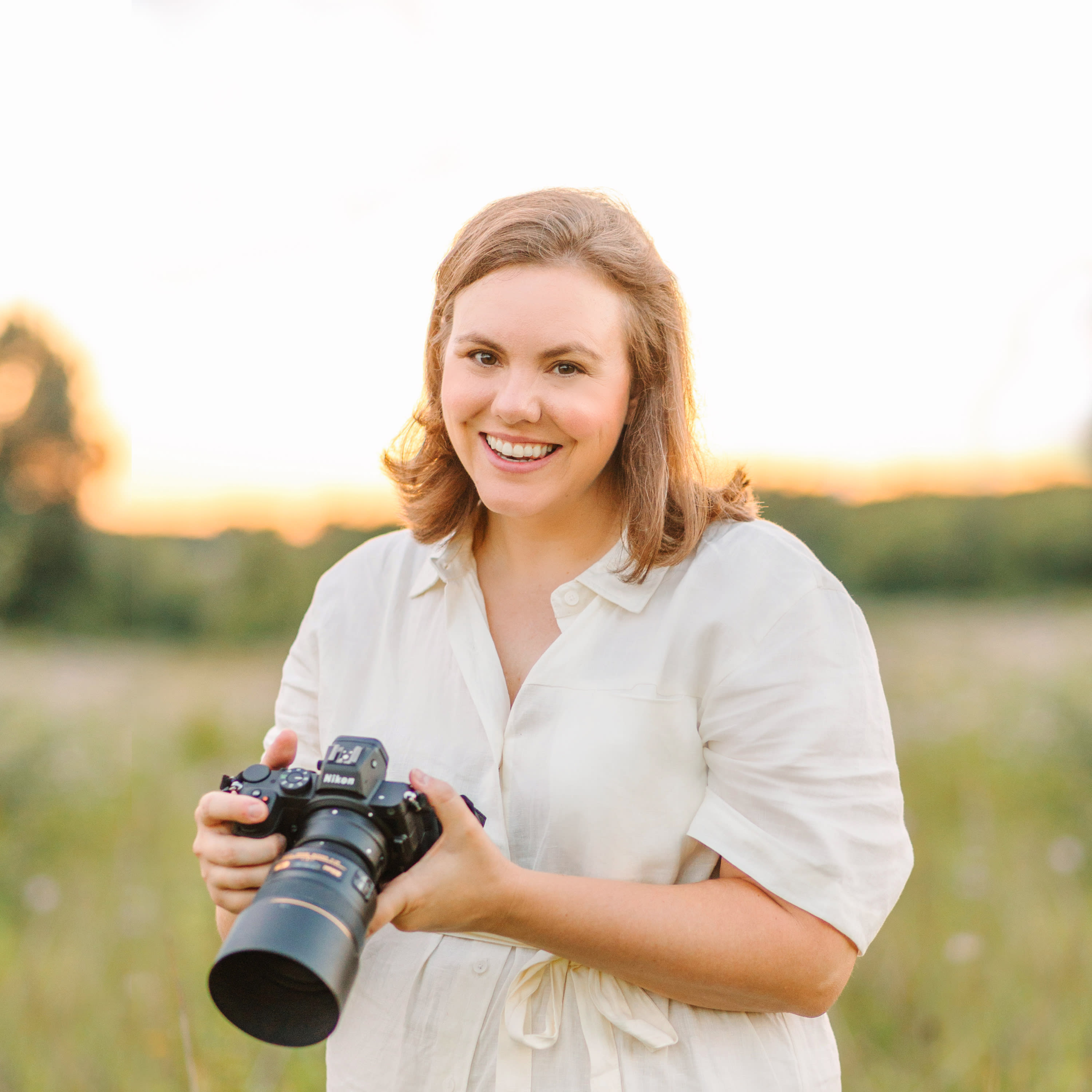 Chicago portrait photographer Kristen Hazelton wearing a white linen dress and holding a camera in a field of wildflowers